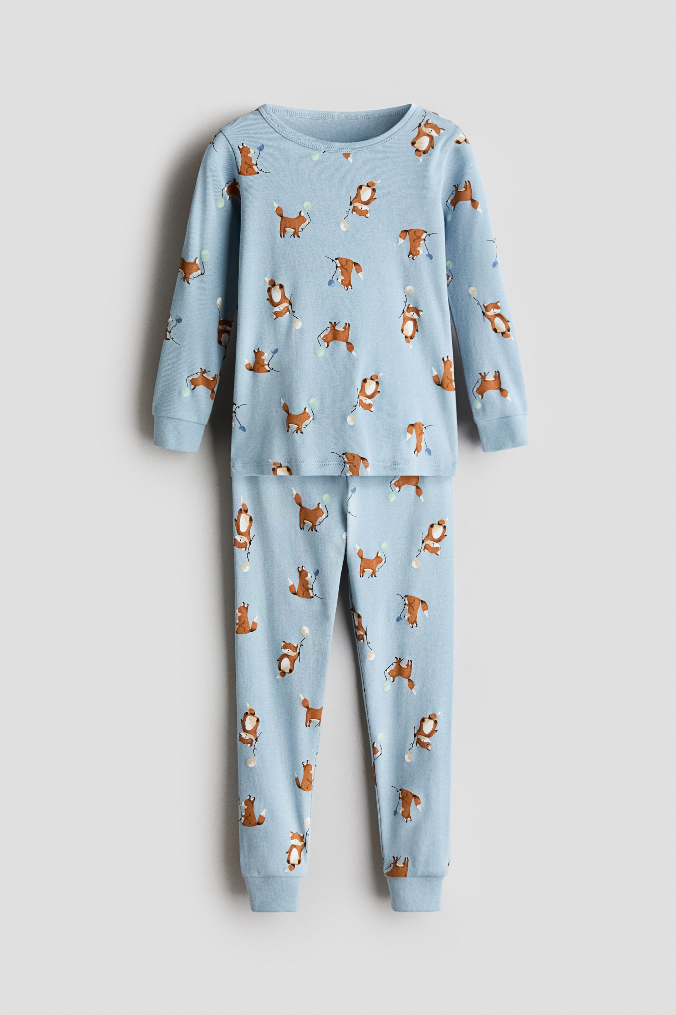 View larger image: Snug-fitting printed pajamas feature a light blue long-sleeved top and matching pants, both displaying a repeating pattern of brown foxes holding balloons. The top has a crew neckline and hemmed cuffs, while the pants feature a close-fitting style with hemmed ankle cuffs.