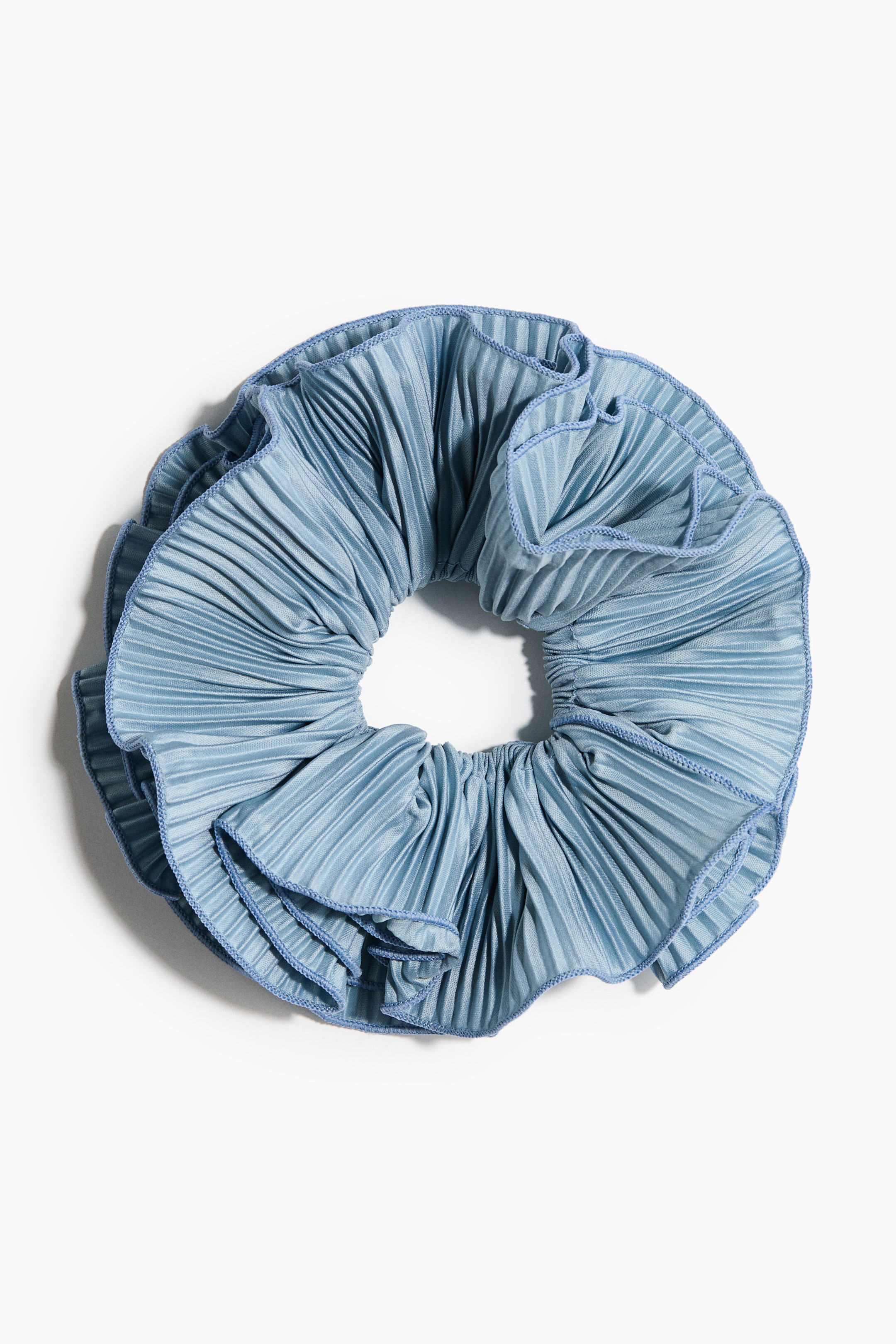 Grotere afbeelding bekijken: Een lichtblauwe geplooide scrunchie ligt plat en toont zijn gerimpelde randen, afgewerkt met een blauw koordbiesje.