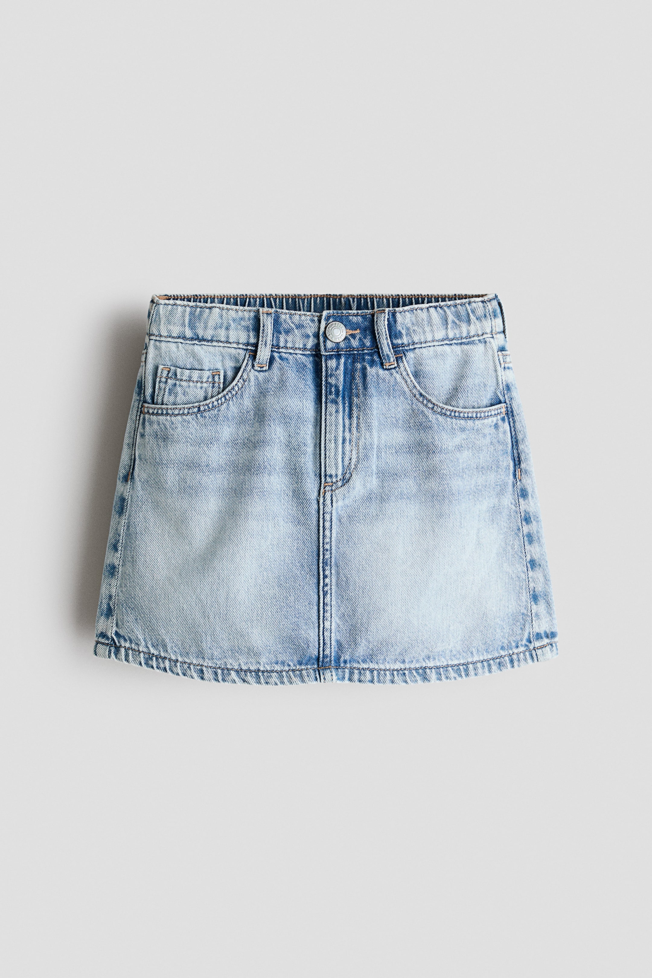 View larger image: This light blue washed cotton denim skirt showcases its front view, highlighting a gathered elastic waistband, button closure, zip fly, and two curved front pockets with a coin pocket.