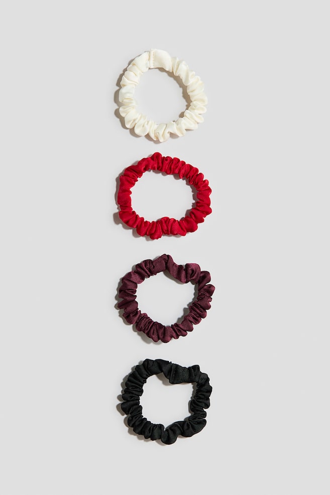 Vier Scrunchies aus gewebtem Stoff mit leichtem Glanz liegen in einer vertikalen Reihe und zeigen ihr gerafftes, gerÃ¼schtes Design. Die Scrunchies sind von oben nach unten in Creme, leuchtendem Rot, dunklem Burgunderrot und Schwarz zu sehen. - 1