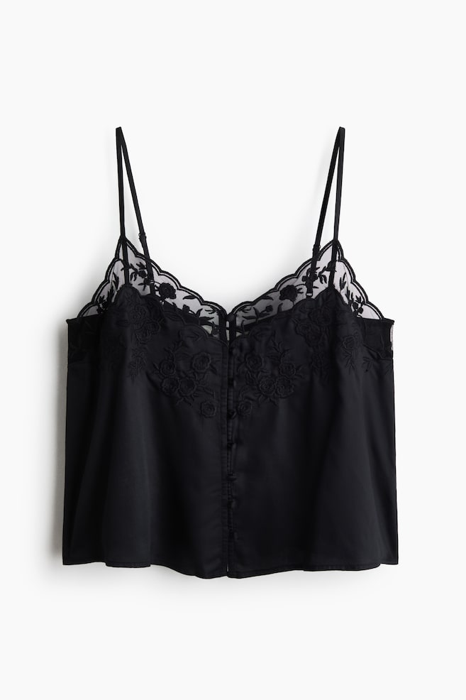 A black woven cami top is shown from the front, featuring a V-shaped neckline with sheer, scalloped floral embroidery. The top is displaying narrow, adjustable shoulder straps, tonal floral embroidery on the chest, and a vertical row of small covered buttons running down the center front. - 1