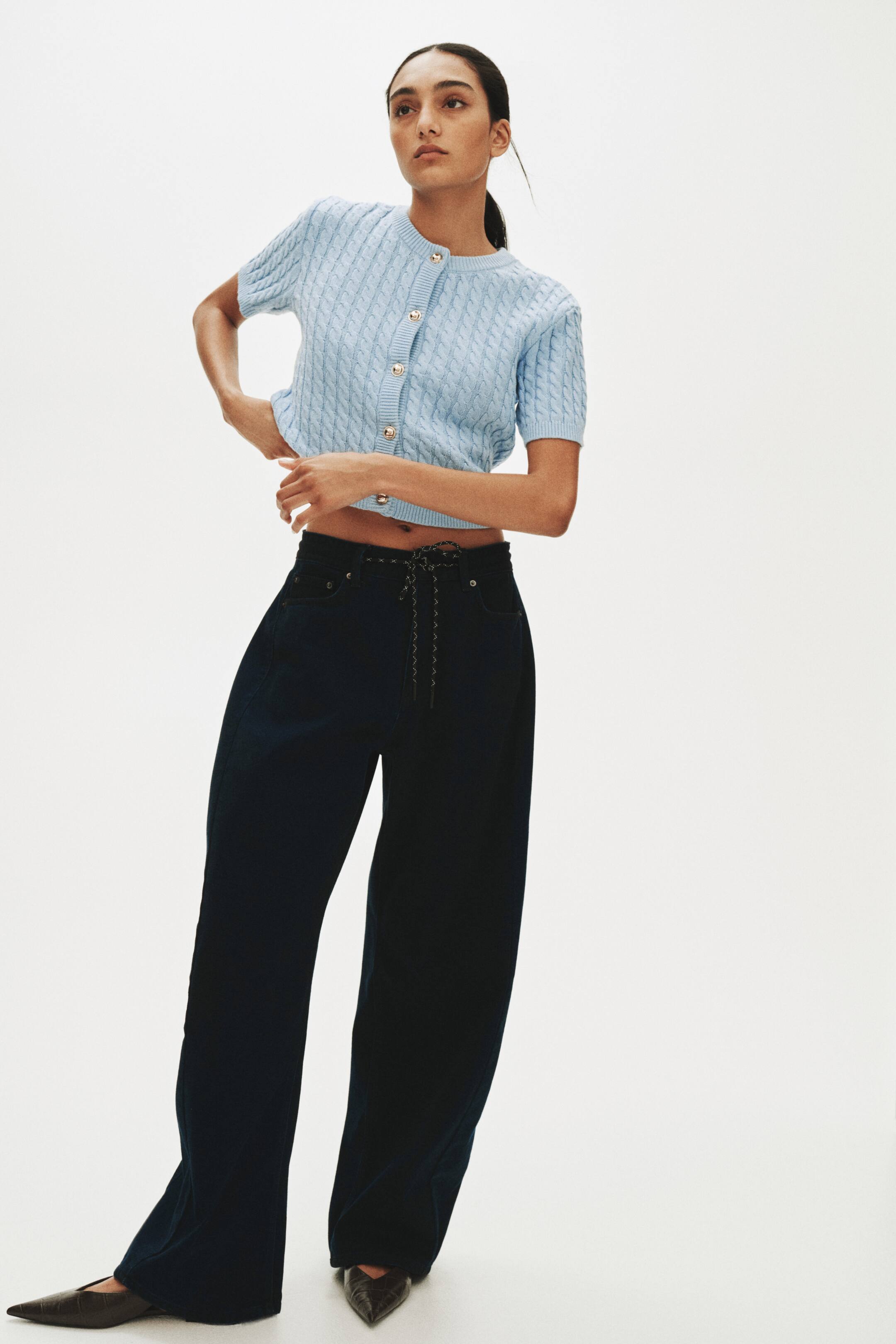 View larger image: A light-blue, short-sleeved cable-knit cardigan is shown from the front, featuring a crew neck, gold-toned buttons down its centre-front closure and a cropped hem.