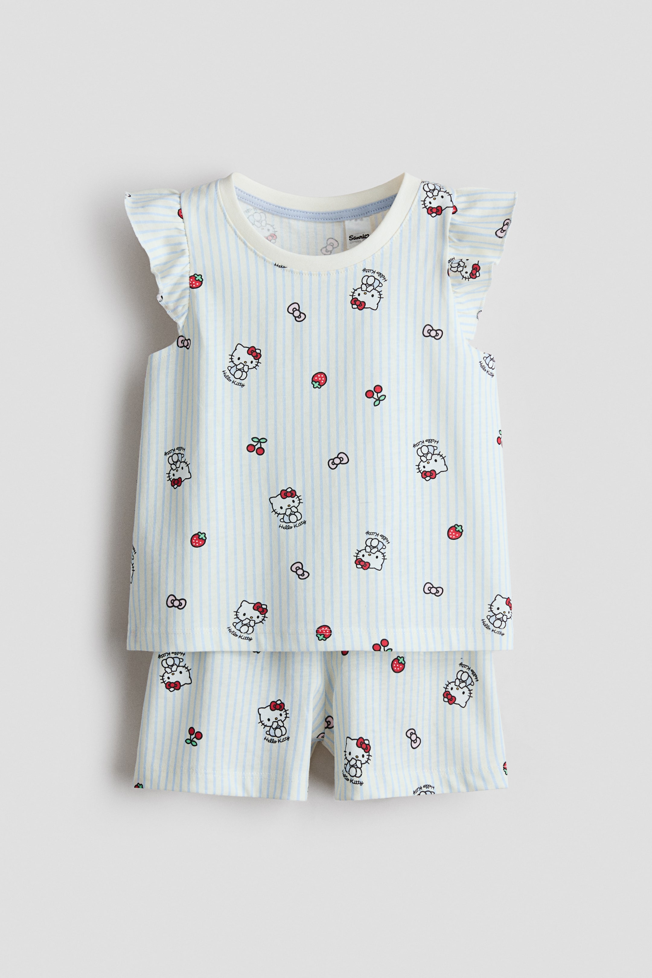 Grotere afbeelding bekijken: Pyjama's in een lichtblauw en wit gestreepte jersey stof worden frontaal gepresenteerd, met een print van Hello Kitty, aardbeien en kersen. Het bovenstuk heeft een ronde halslijn en vlindermouwen, en de shorts zijn ontworpen met een bedekte elastische tailleband.