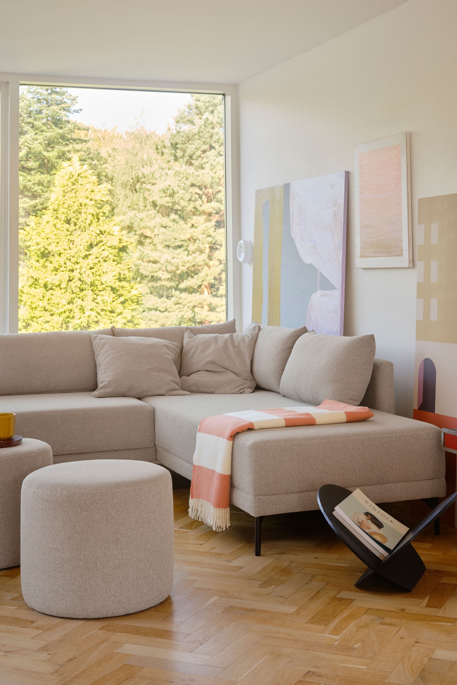 Ein hellbeiges, gepolstertes Ecksofa prÃ¤sentiert eine L-fÃ¶rmige Konfiguration mit einer langen, rÃ¼ckenfreien BankverlÃ¤ngerung auf der linken Seite und weichen RÃ¼ckenlehnenkissen auf der rechten Seite. Das Sofa steht auf dÃ¼nnen, schwarzen Metallbeinen und ist leicht nach links gedreht, um seine klaren Linien und das niedrige Profil zu zeigen.