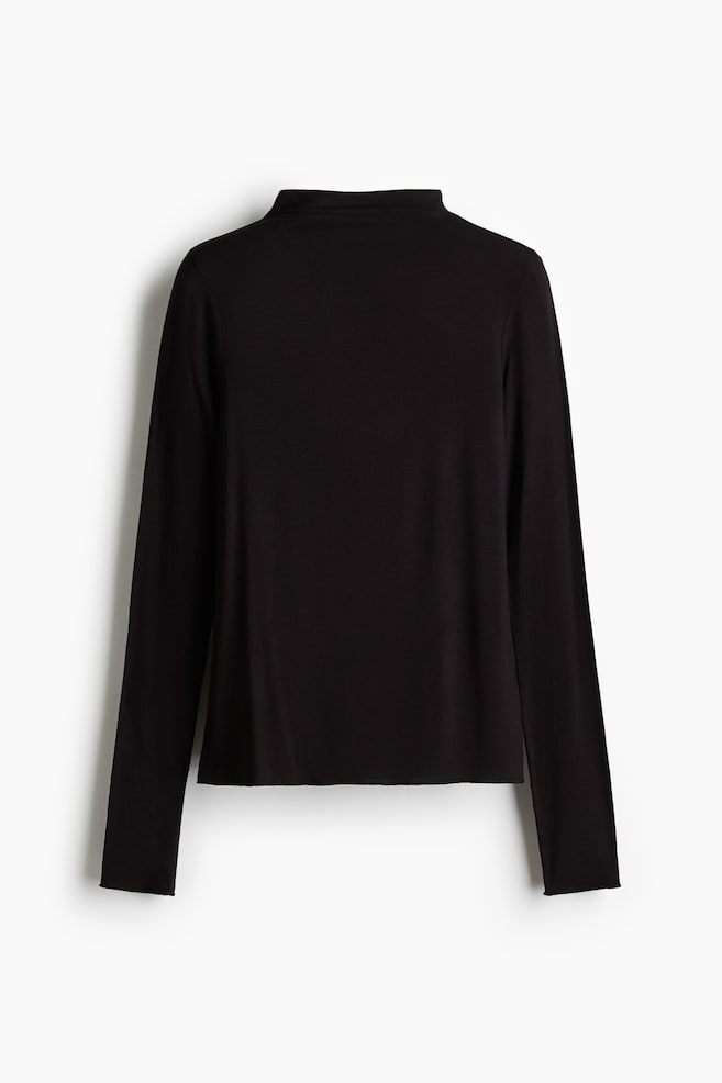 A black jersey top is being presented from the back, featuring a turtleneck and long sleeves. Overlocked edges are visible at its cuffs and hem. - 1