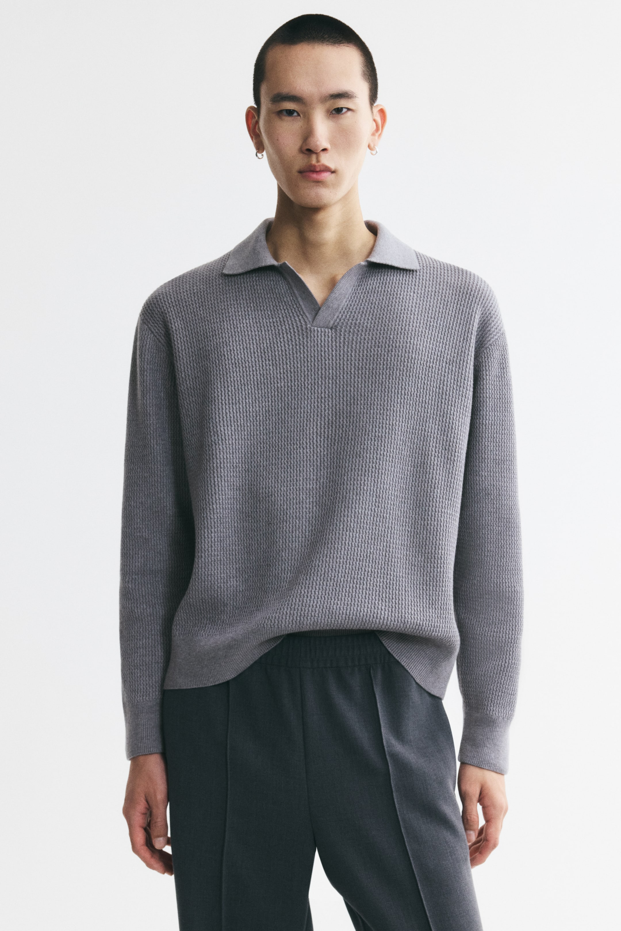 View larger image: A grey textured knit polo shirt with an open collar, long sleeves, and ribbed cuffs and hem is being worn by the model. The shirt is displaying a relaxed fit and is paired with dark grey pants.