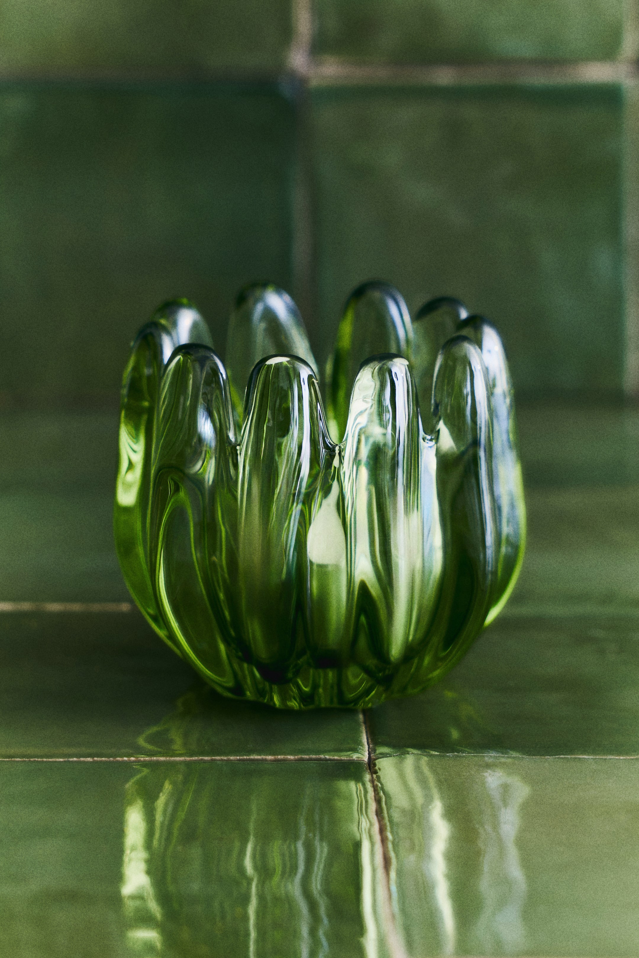 View larger image: "A translucent green glass tealight holder showcases a petal-inspired design with undulating lobes forming its sides, as viewed from the front. A white tealight candle rests inside."