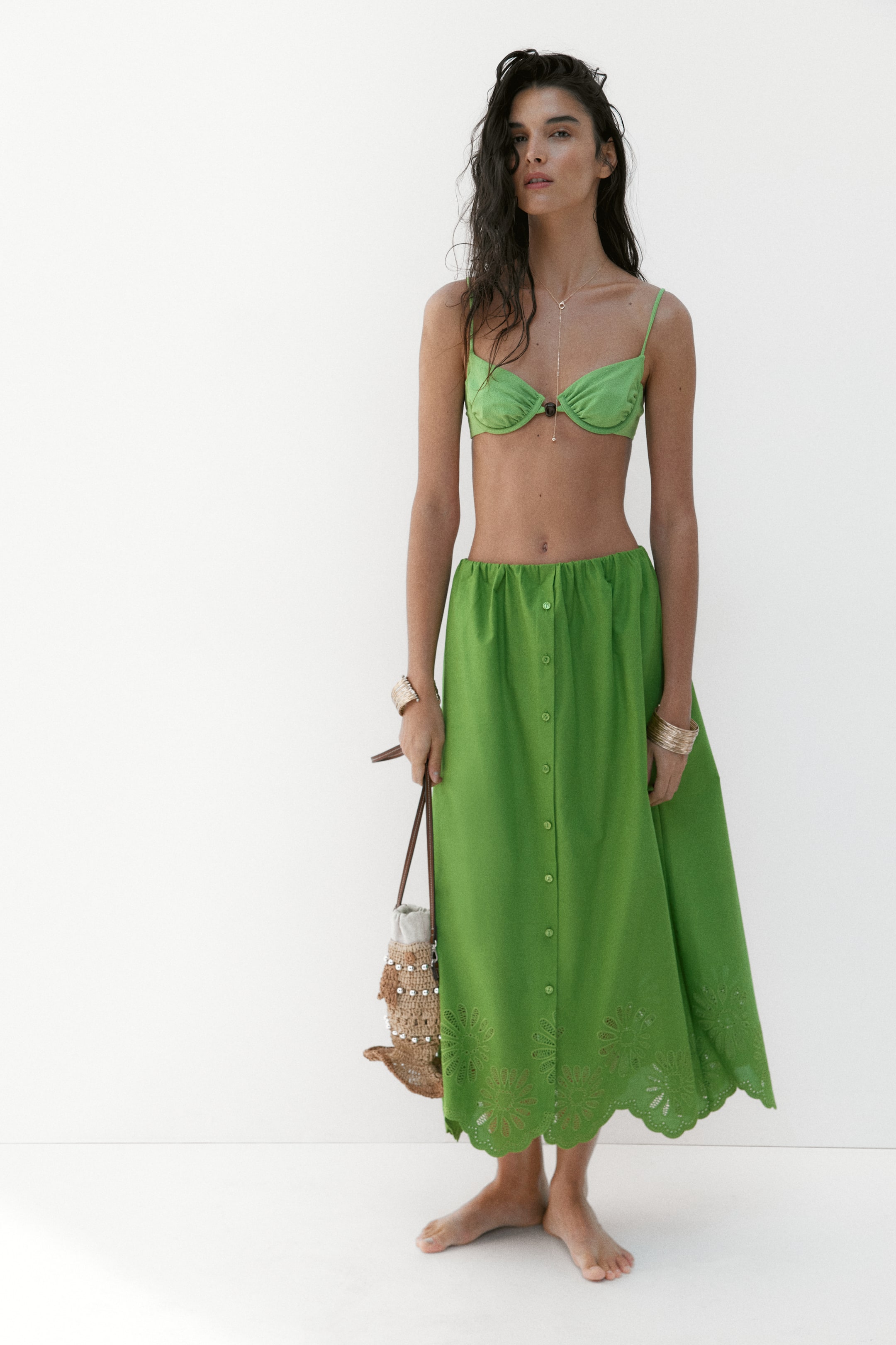 Προβολή μεγαλύτερης εικόνας: Ένα φωτεινό πράσινο σετ δύο κομματιών παρουσιάζεται, με ένα σουτιέν μπικίνι με μπανέλα και λεπτές τιράντες. Η αντίστοιχη midi φούστα είναι σχεδιασμένη με μια πλήρη σειρά κουμπιών μπροστά και ένα κυματιστό στρίφωμα διακοσμημένο με κεντήματα λουλουδιών με κοψίματα.