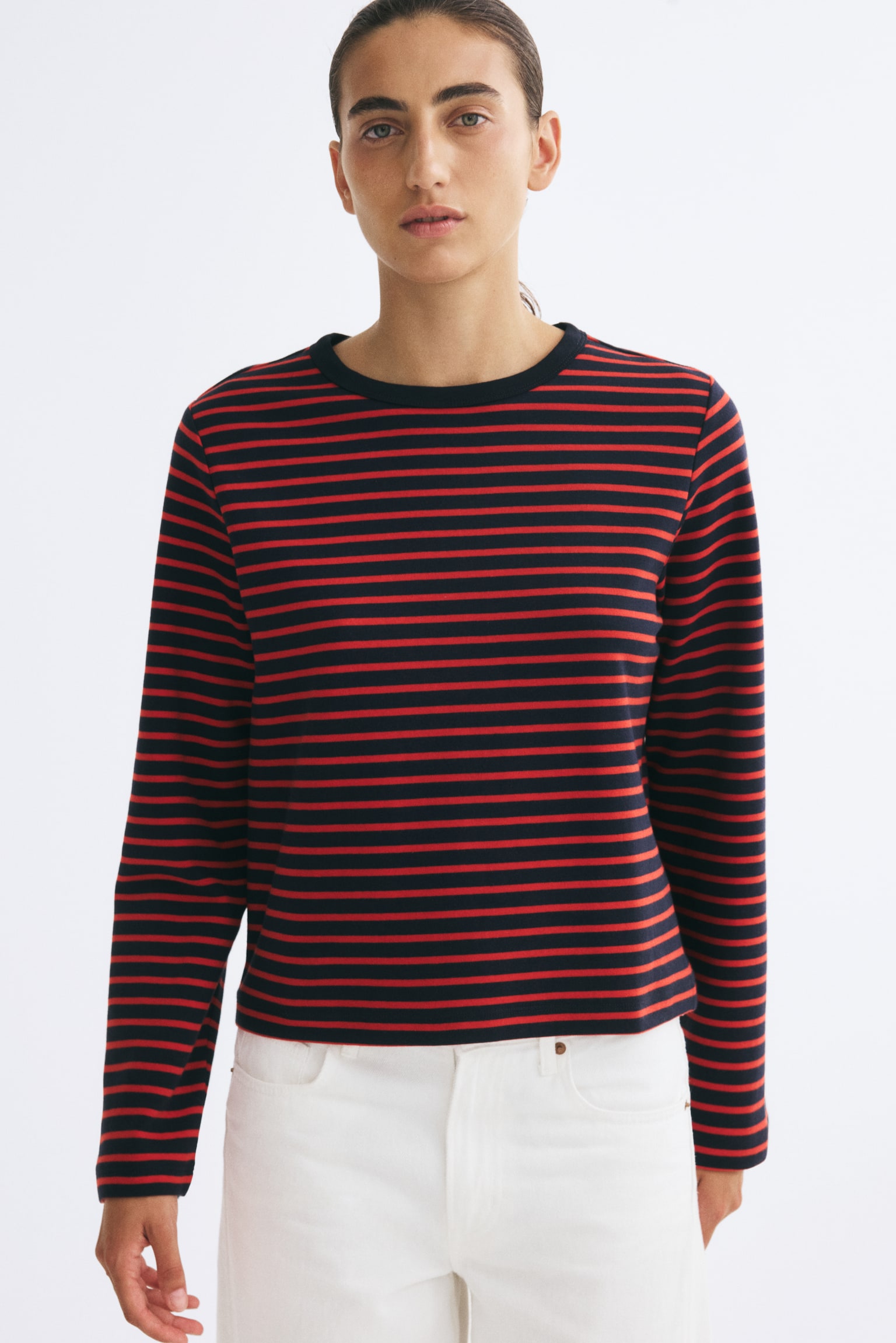 A heavy jersey top with horizontal red and navy blue stripes, a round rib-trimmed neckline, and long sleeves is worn by the model. The top is paired with white trousers. - 1