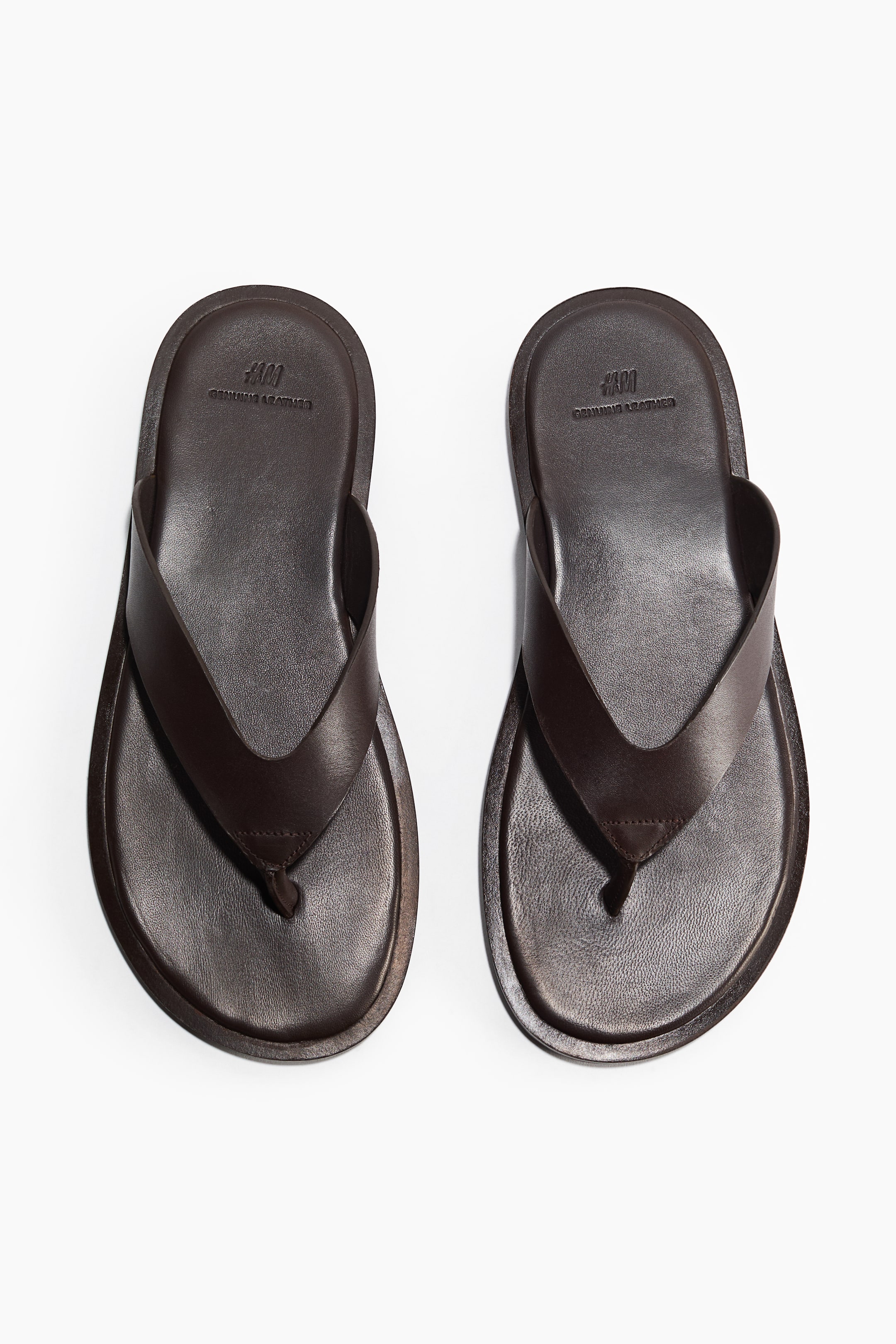 View larger image: A pair of dark brown leather flip-flops is displayed from a top-down perspective, showcasing round toes, wide straps, and a narrow toe post.