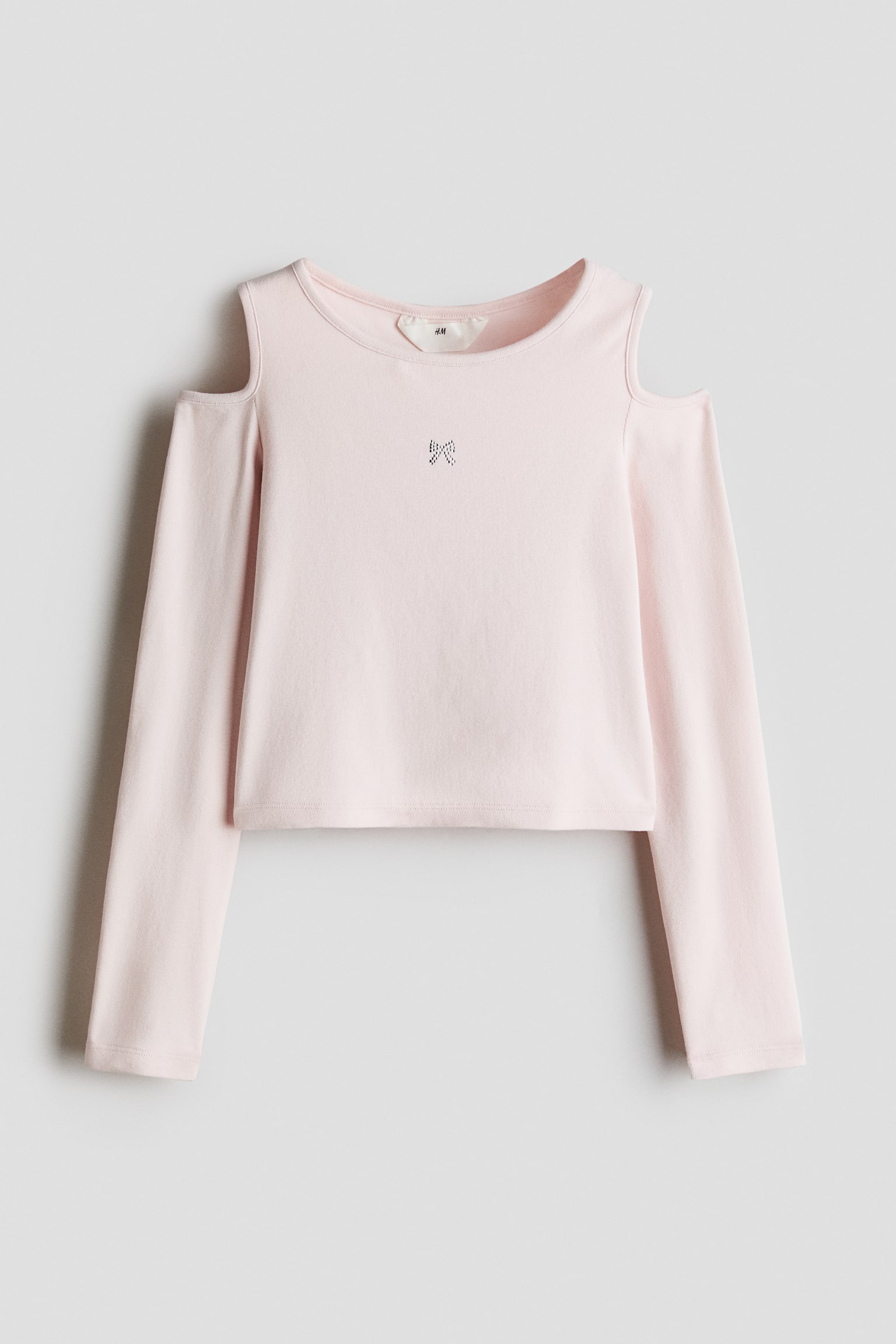 A light pink, long-sleeved top features cold-shoulder cutouts and a crew neckline. A small rhinestone bow detail embellishes the centre of the chest on the slightly cropped bodice.