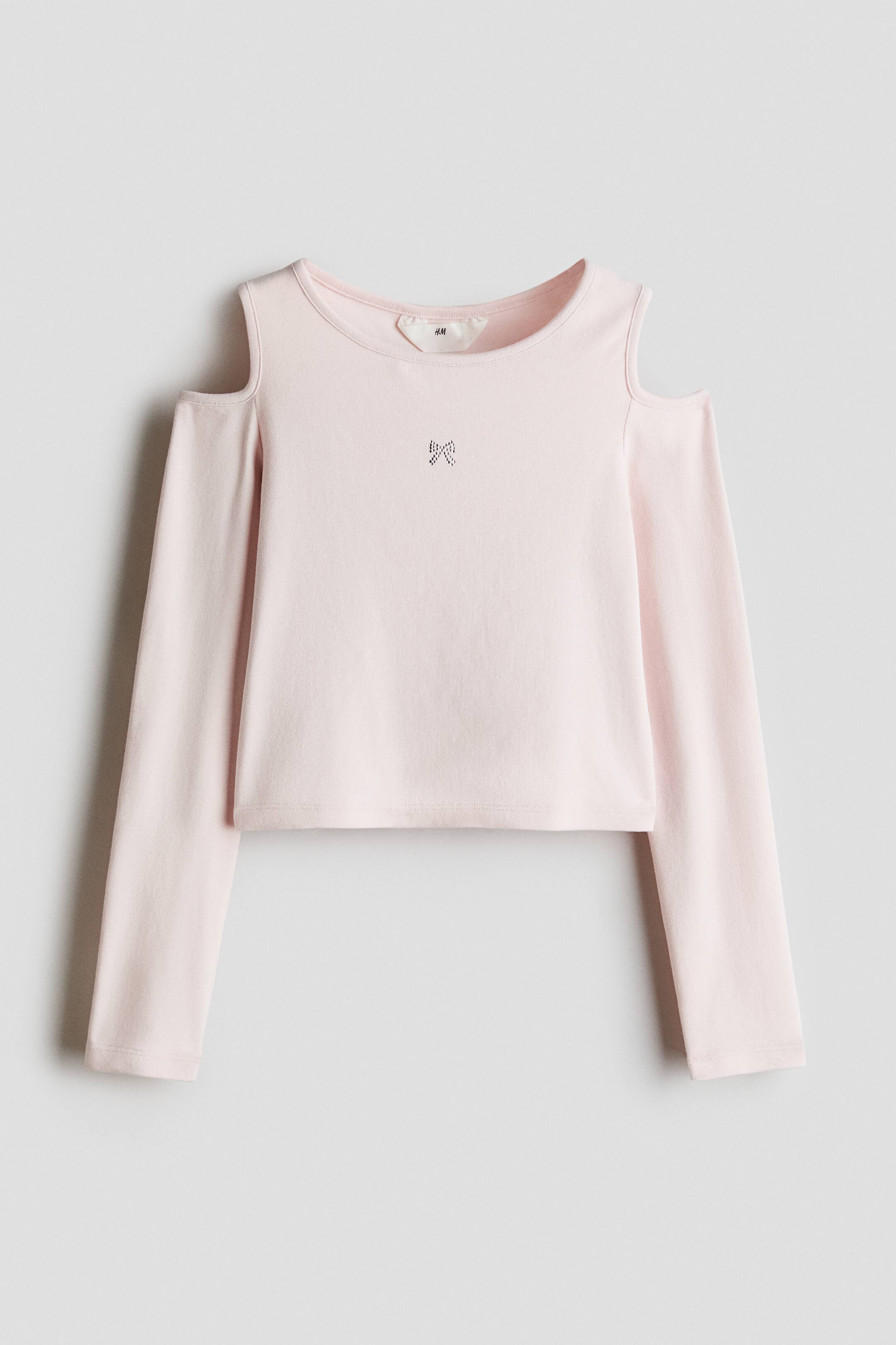View larger image: A light pink, long-sleeved top features cold-shoulder cutouts and a crew neckline. A small rhinestone bow detail embellishes the centre of the chest on the slightly cropped bodice.
