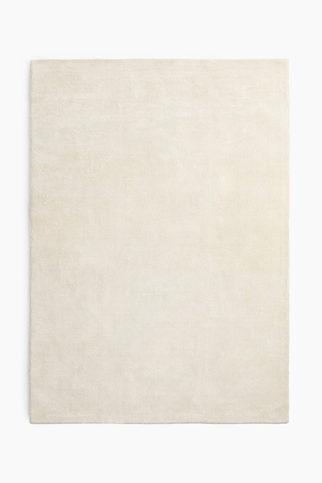 A rectangular rug showcases a light beige hue with a subtle, consistent texture across its flat surface. - 1