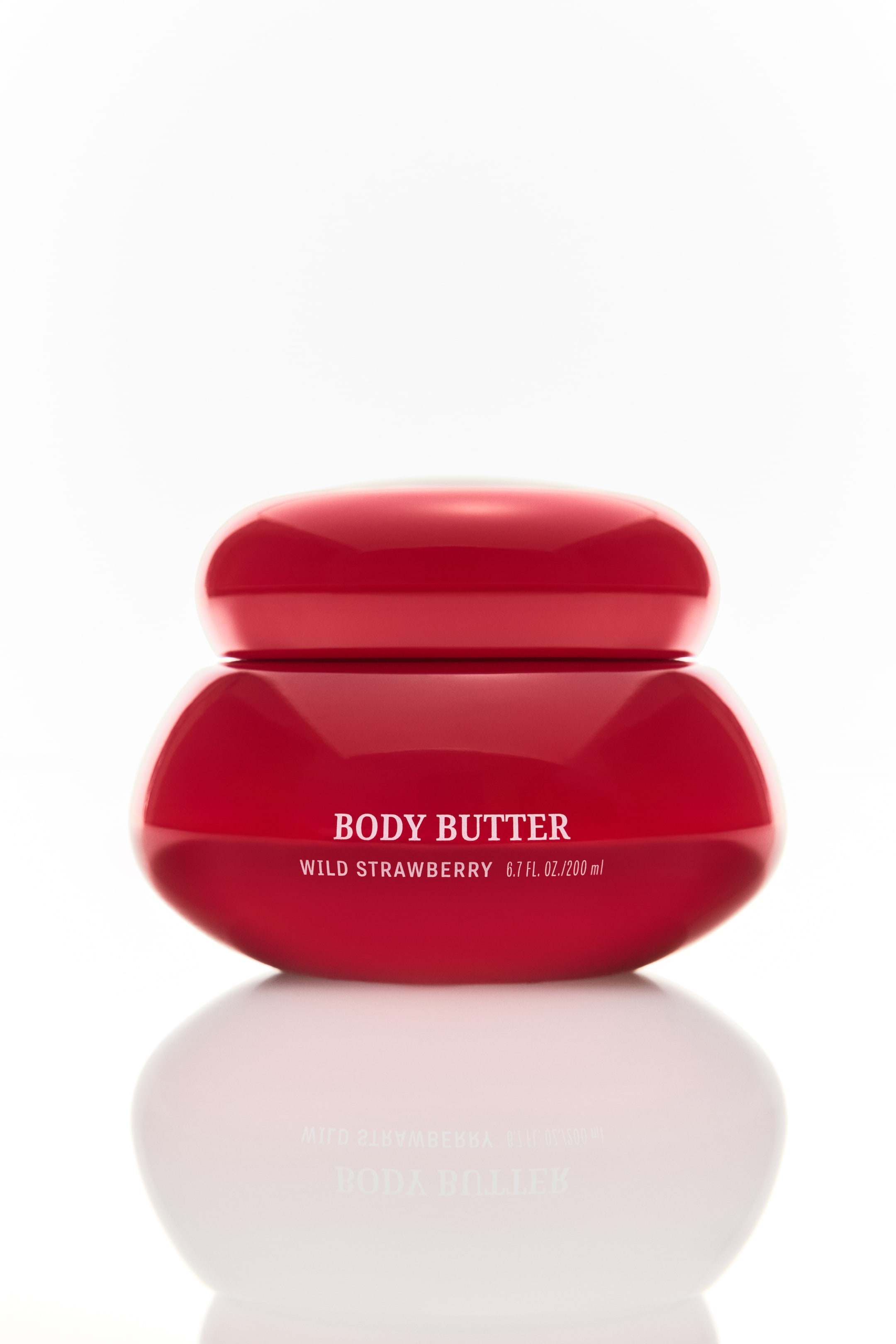 View larger image: A glossy red body butter jar stands upright, facing forward. It features a rounded, bulbous shape with a matching rounded lid, and white text on the front reads "BODY BUTTER," "WILD STRAWBERRY," and "6.7 FL. OZ. / 200 ml."
