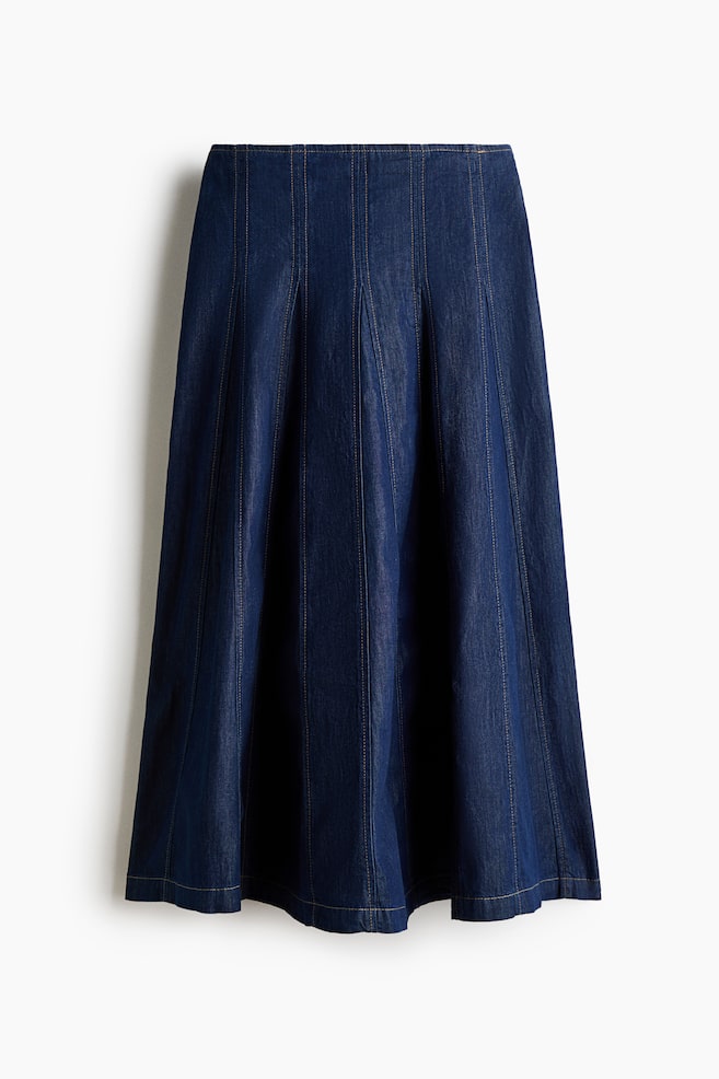 A dark blue denim midi skirt is shown from the front, featuring fitted vertical panels with contrasting topstitching that flare into godet pleats towards the hem. - 1
