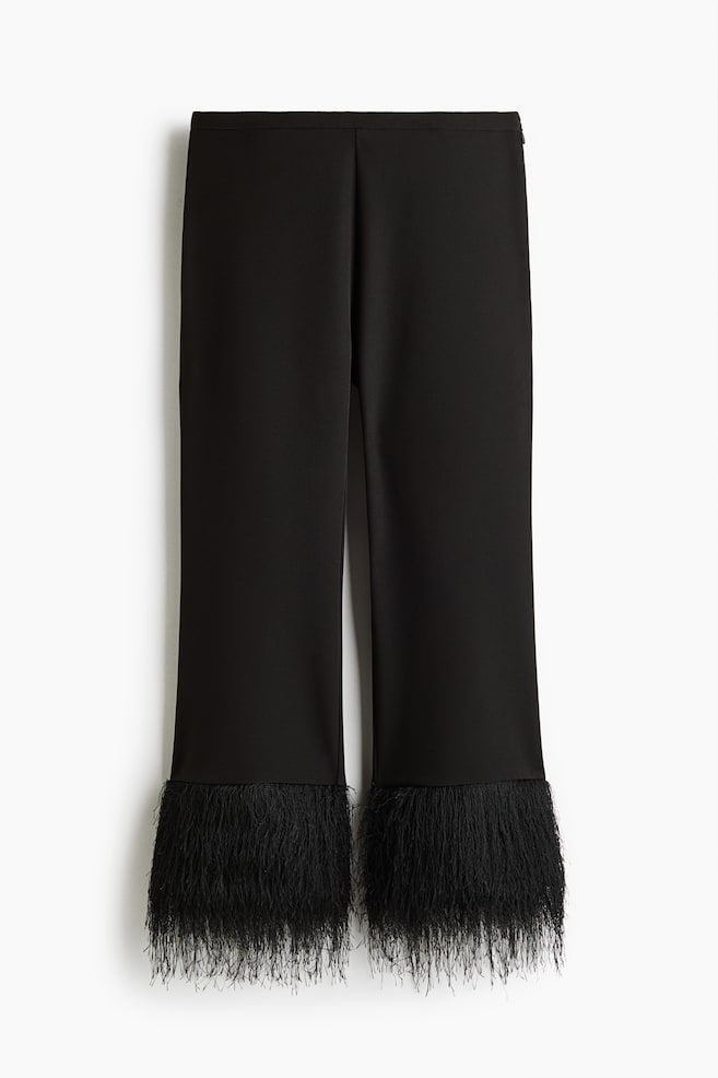 These black cropped trousers are hanging front-facing, featuring a smooth, flat waistband and straight-cut legs finished with dense, textured black feather trim at the hems. - 1