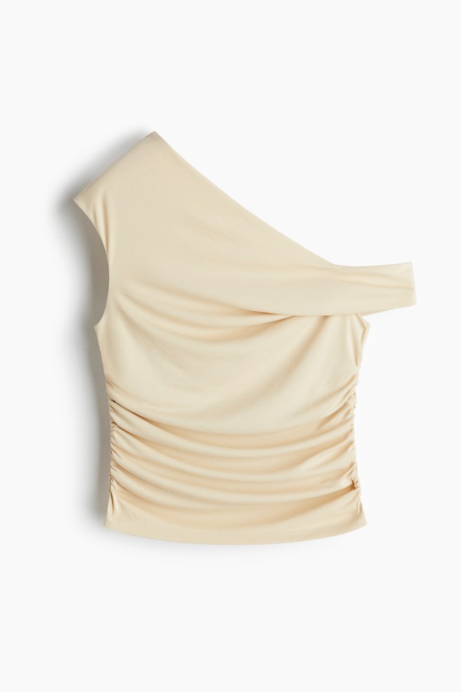 A light beige one-shoulder top is displaying from the front, featuring a draped neckline on its right side and a sleeveless left side, with extensive vertical ruching appearing on its lower body. - 1