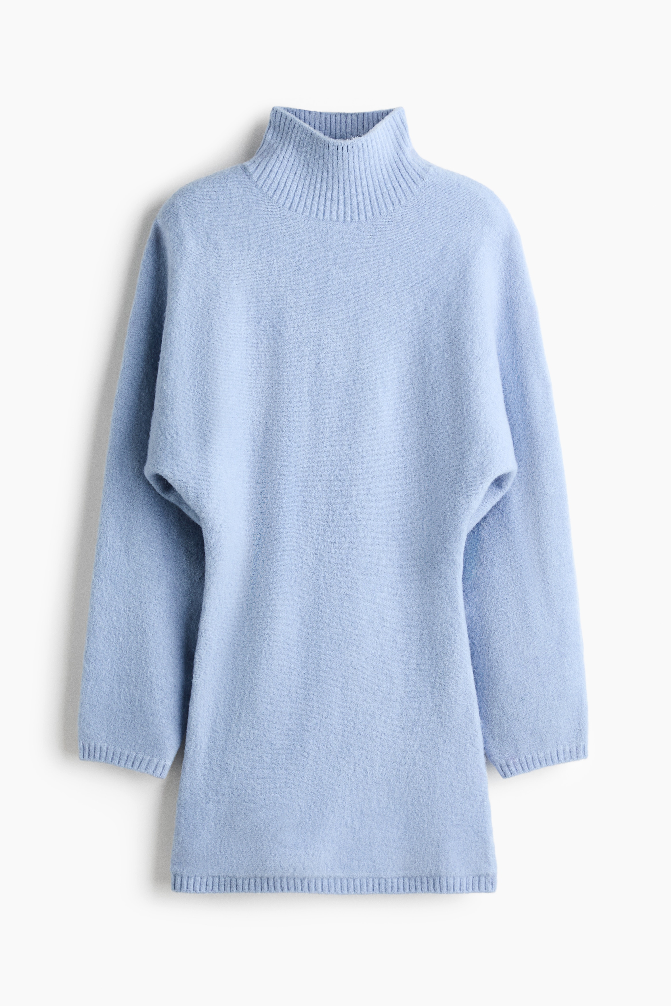 A light blue, soft knit mini dress is being worn by the model, featuring a high ribbed neck, long dolman sleeves, and a fitted skirt with a ribbed hem. A brown and black plaid shirt is tied around the waist of the dress, which is styled with white socks and sneakers.