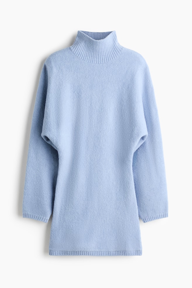 A light blue knit tunic sweater is hanging facing the front, featuring a high ribbed mock neck, relaxed dolman-style sleeves with ribbed cuffs, and a straight ribbed hem. - 1
