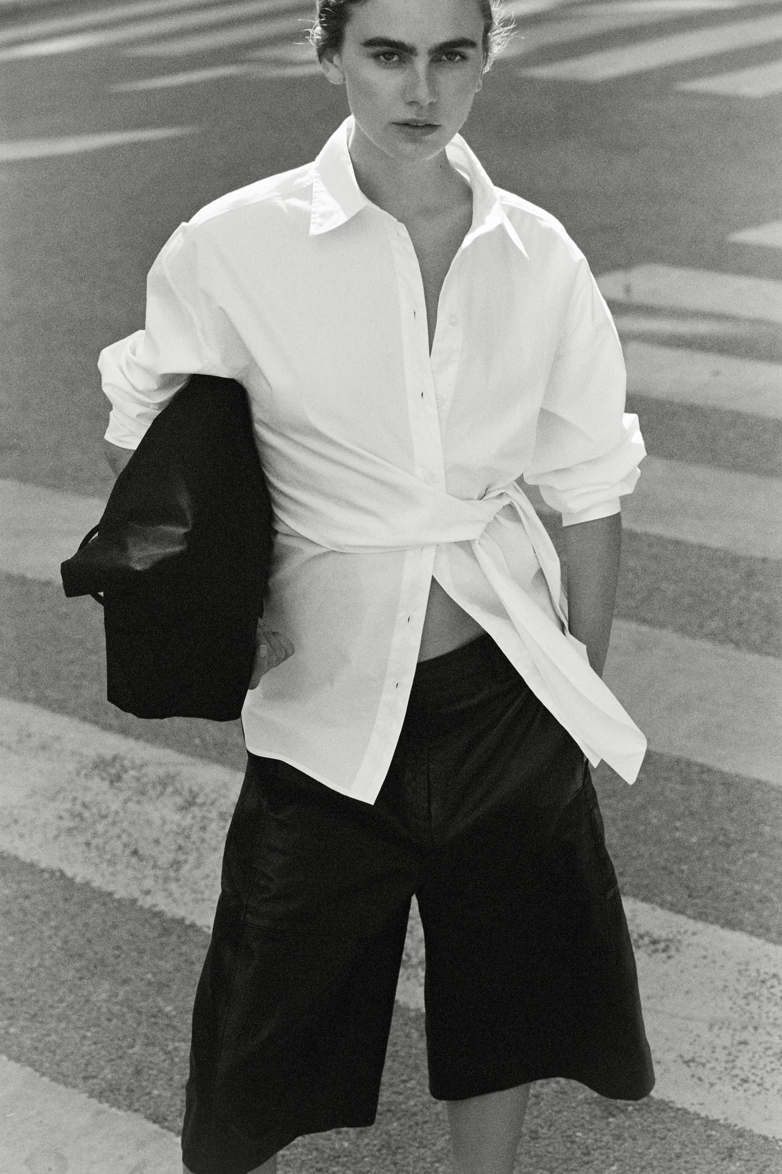 A white long-sleeved shirt featuring a pointed collar and a front button placket, with a fabric panel wrapping from the left side and tying into a knot at the right hip. - 1