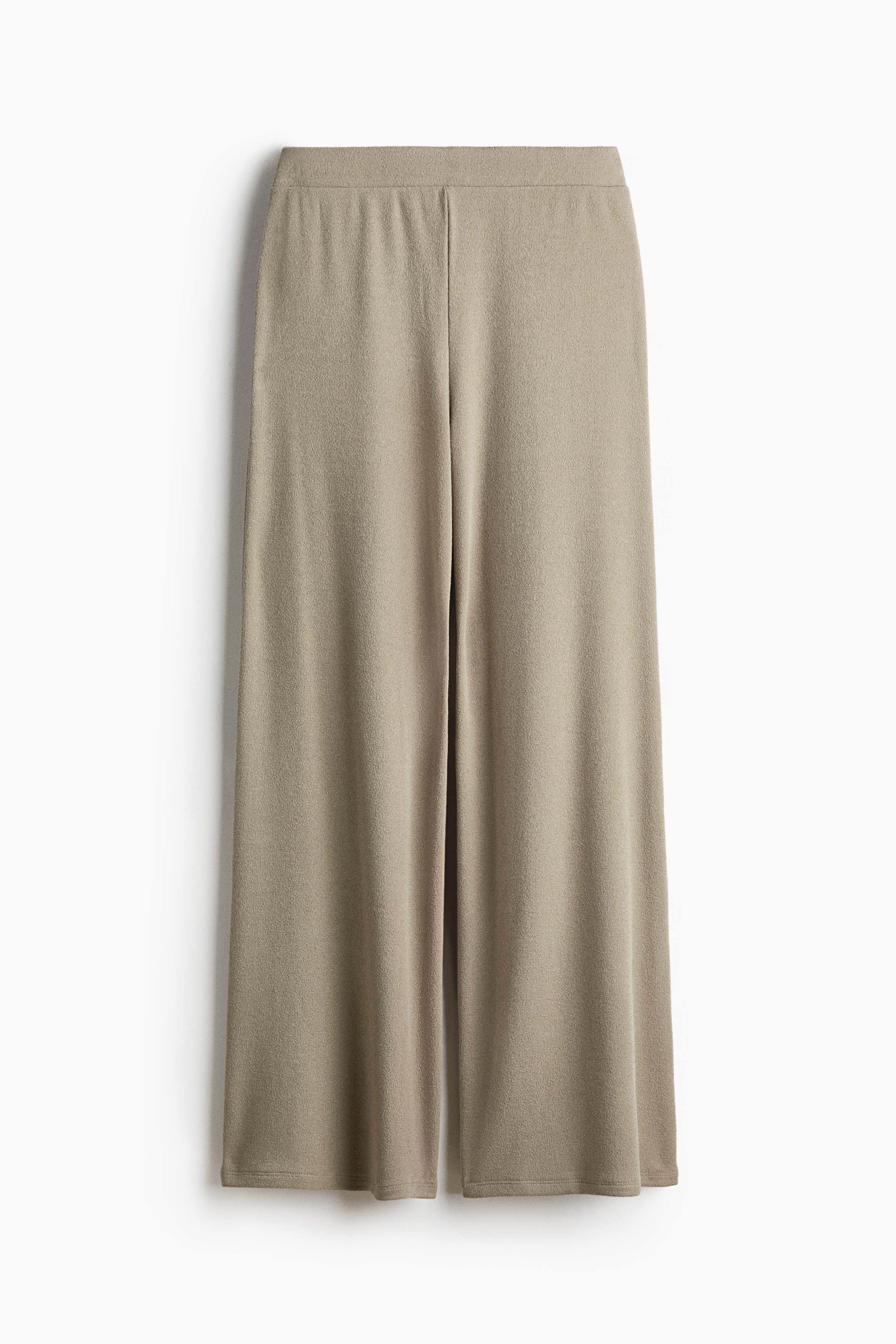 Loose-fit, beige ribbed jersey trousers featuring a regular waist and straight legs are being worn by the model. The trousers are styled with a matching short-sleeved ribbed top and black sandals.