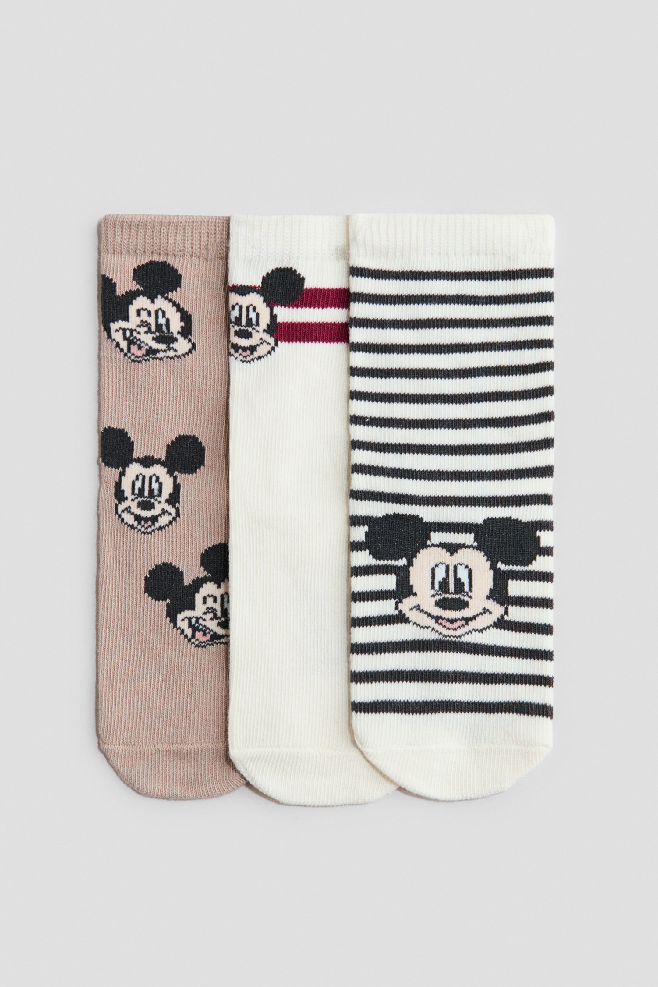 View larger image: A set of three socks is laid flat, each sock showcasing a unique Mickey Mouse design. The first sock features repeating Mickey Mouse faces on a light brown backdrop. The second sock displays a single Mickey Mouse face accompanied by two burgundy stripes on an off-white background, while the third sock presents black horizontal stripes with a single Mickey Mouse face on an off-white background.