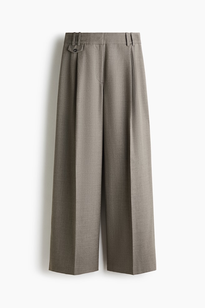 These wide-leg, high-waisted trousers in a taupe wool blend are shown from the front, featuring a structured waistband with belt loops, deep front pleats, and sharp pressed creases running down each leg. A small coin pocket with a buttoned flap is visible on the right hip, highlighting the tailored construction. - 1