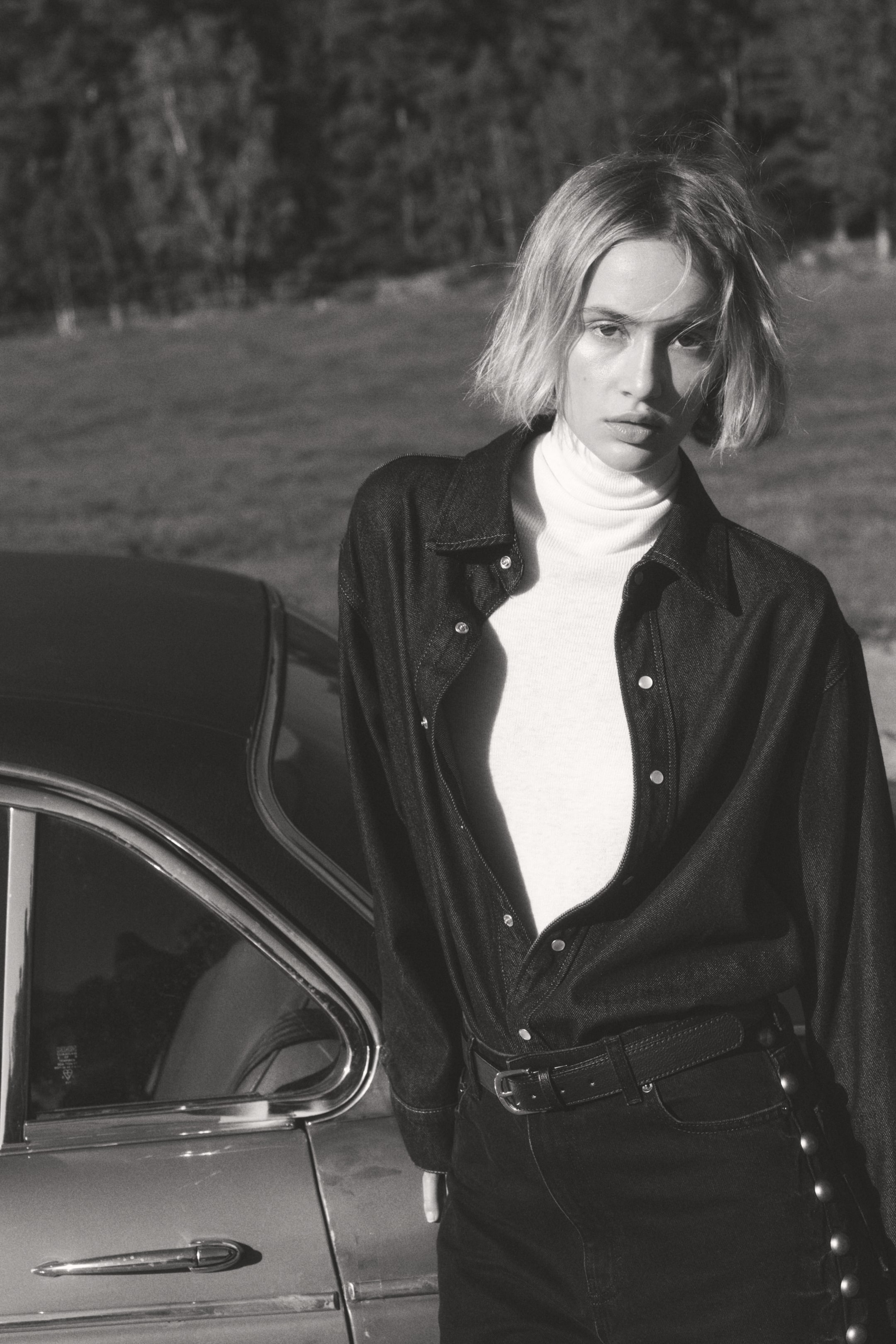 Voir une image plus grande: Le mannequin porte un jean à cinq poches en denim de coton rigide, avec une taille régulière, une braguette zippée avec bouton, et des jambes droites ornées de clous métalliques en forme de dôme sur les côtés extérieurs. Une ceinture est portée à travers les passants du jean.