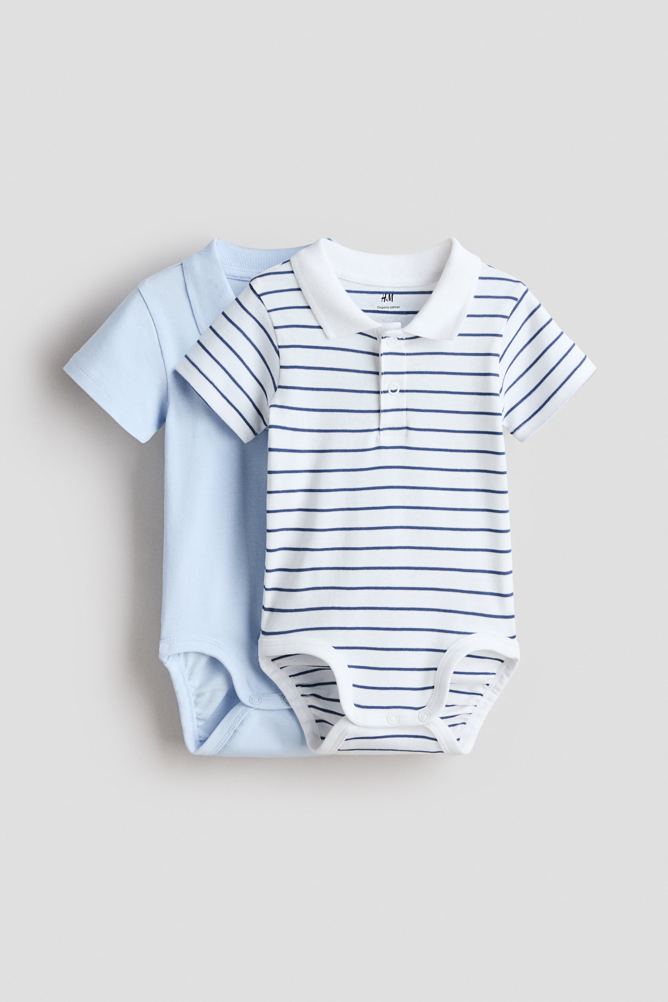 View larger image: Two polo-style bodysuits are showcased from the front, one in a solid light blue hue and the other in white adorned with navy blue horizontal stripes. Both garments feature a ribbed collar, a visible press-stud placket, short sleeves, and snap closures at the crotch.