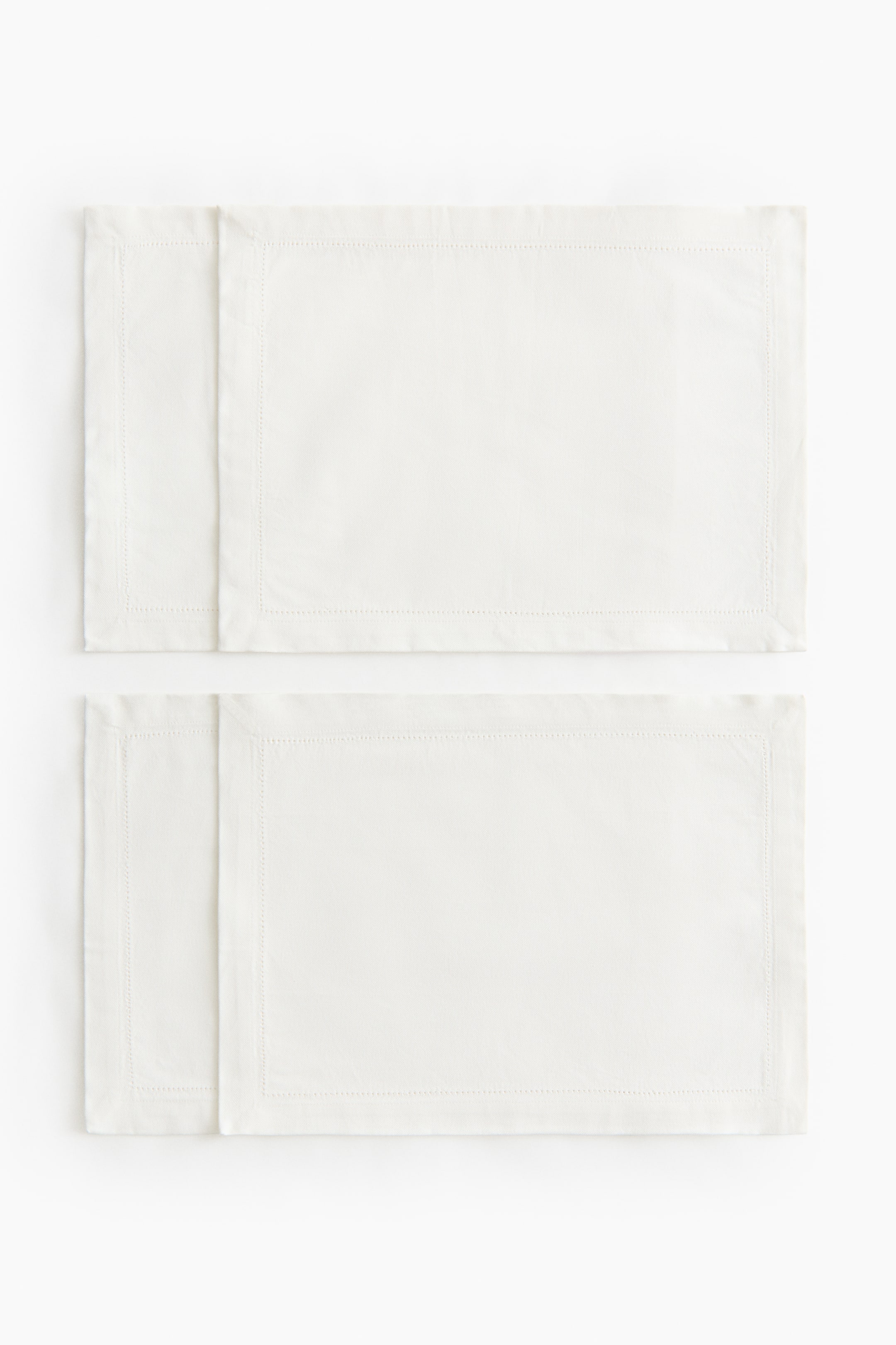 Agrandir l'image: Deux sets de table rectangulaires sont présentés de face. Ils sont confectionnés en toile de coton couleur crème, chaque set de table étant orné d’un point d’ourlet le long de ses bords ourlés, formant une bordure intérieure distincte.