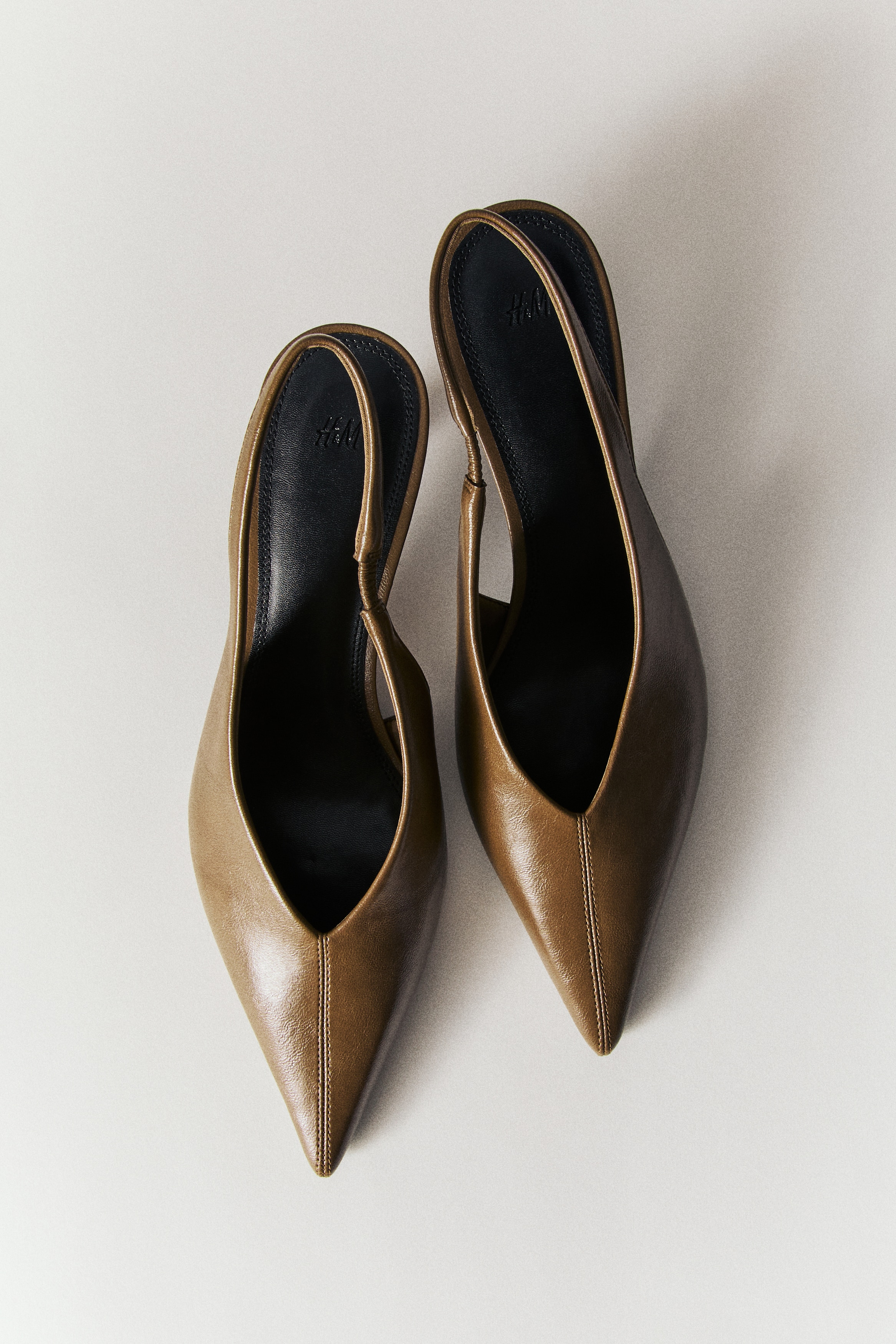 Giày cao gót slingback màu xanh ô liu có mũi nhọn và gót thấp mảnh mai. Sản phẩm này có chất liệu bên ngoài có kết cấu và dây mỏng kéo dài quanh phía sau.