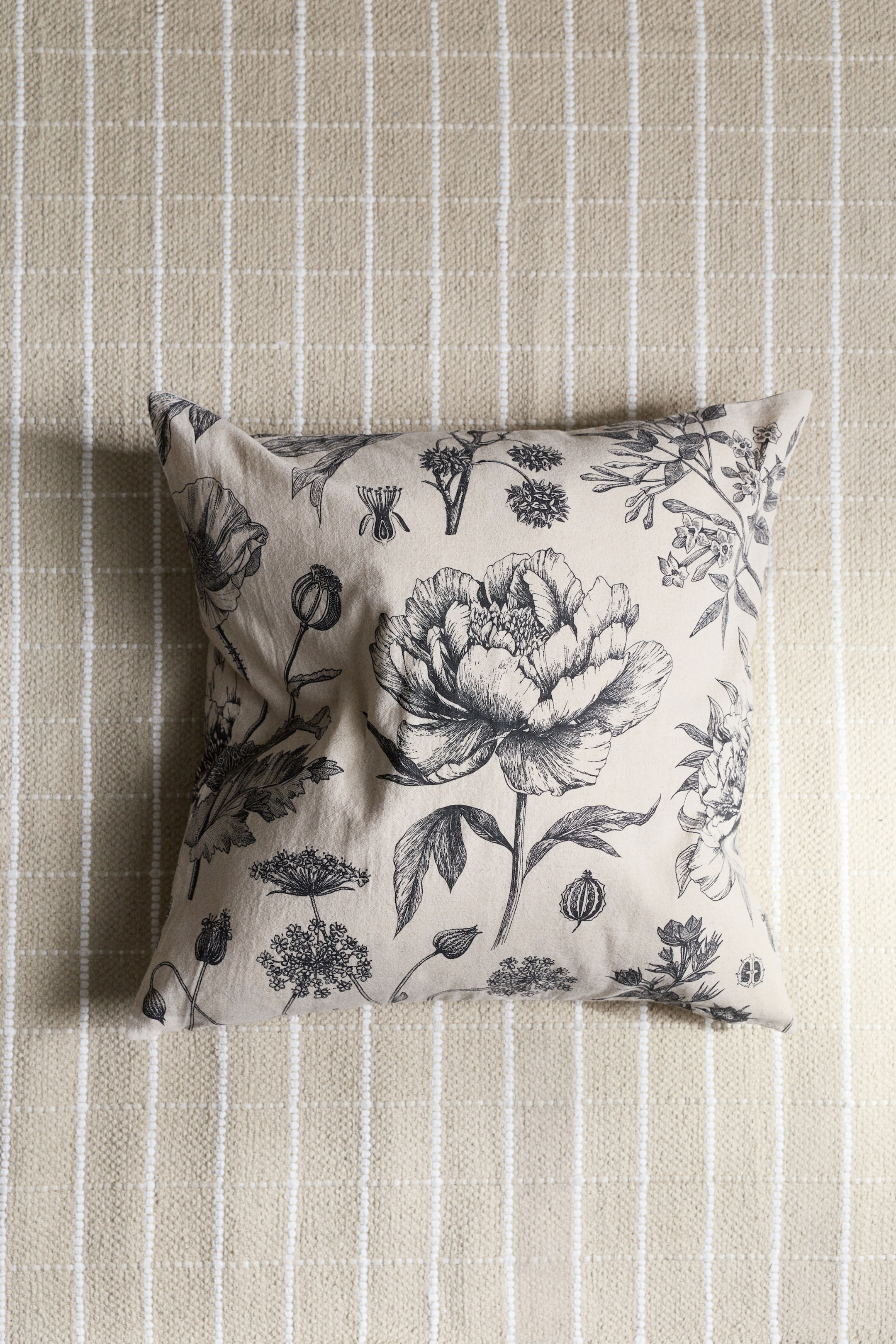 View larger image: This cushion cover, crafted from a woven blend of cotton and linen, showcases an intricate black and white floral pattern on its front. A zipper is neatly positioned along one side of the cover.