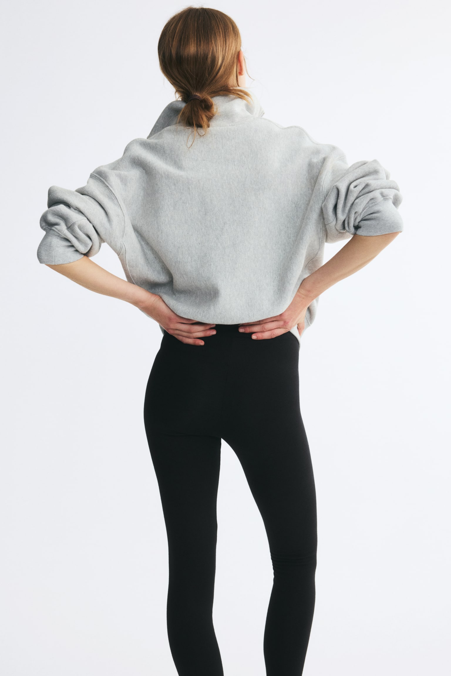 The model is wearing black high-waisted leggings, shown from the rear. The leggings are styled with a grey sweatshirt, with the modelâs hands resting on her lower back to highlight the wide, elasticated waistband. - 1