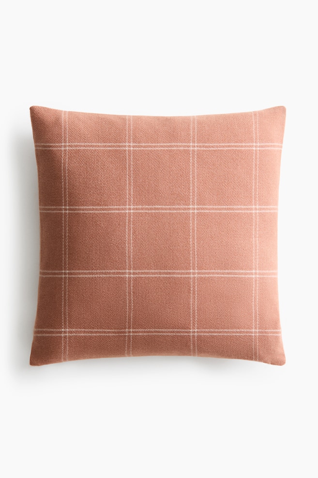 Une housse de coussin carrée est présentée de face, arborant une texture tissée feutrée. Elle affiche une couleur terre cuite atténuée, ornée de lignes claires formant une grille sur sa surface. - 1