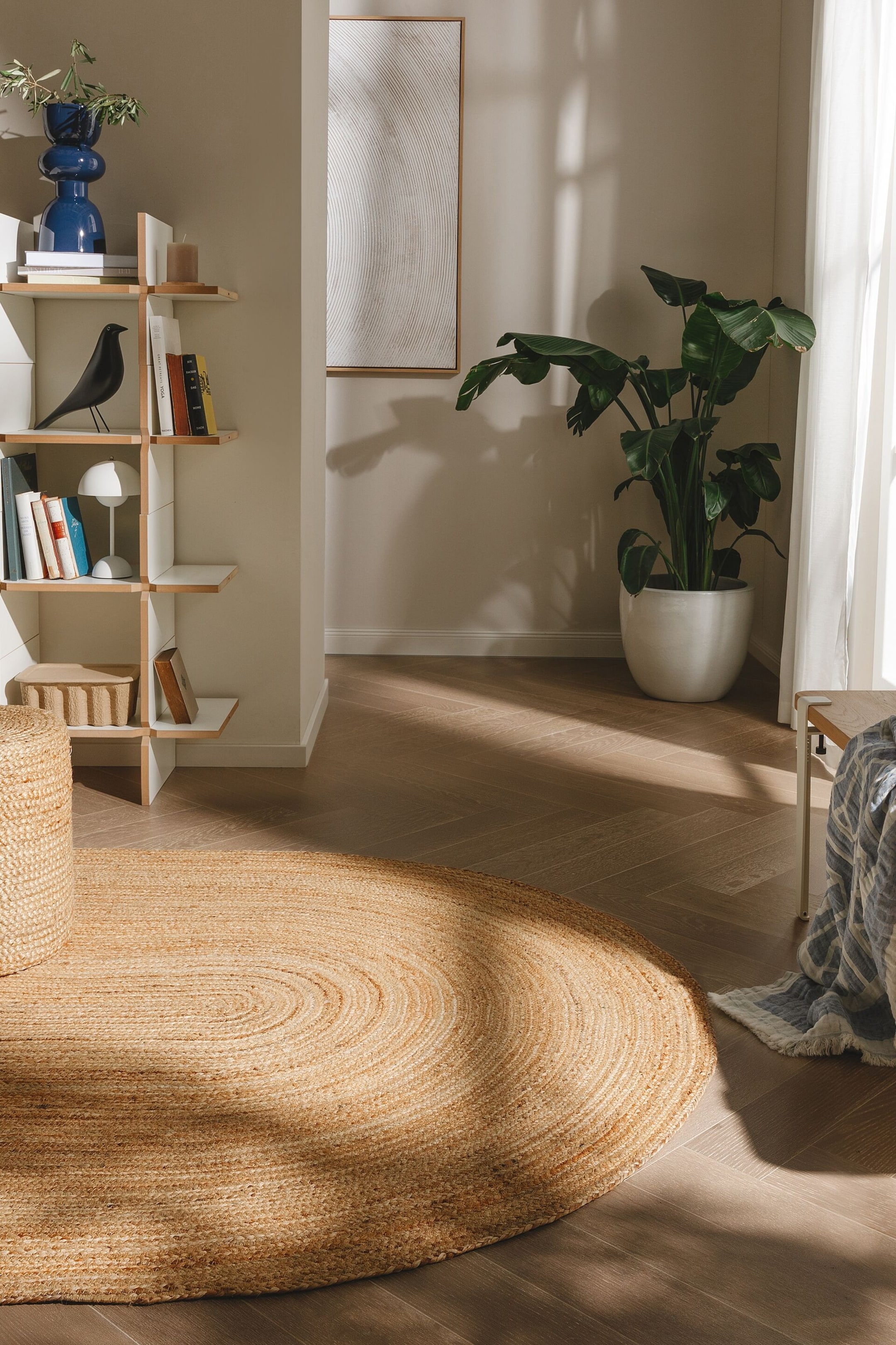 Agrandir l'image: Un tapis ovale en jute est posé à plat sur le sol, s'étendant du bas à gauche jusqu'au centre-droit. Il présente une construction tressée avec des ovales concentriques dans une couleur brun clair naturel.