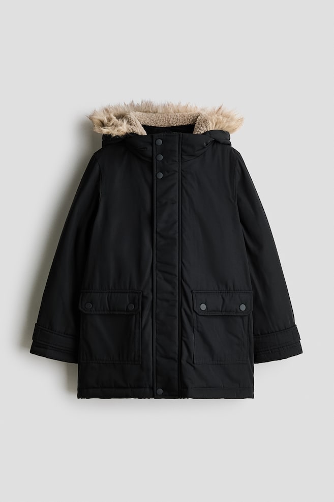 A black padded parka is shown from the front, featuring a high funnel collar and a detachable hood with light beige faux-fur trim and a warm fleece lining. The parka is designed with a concealed front zip beneath a press-stud storm flap, two large front flap pockets with press-stud fastenings, and long sleeves with detailed cuffs. - 1