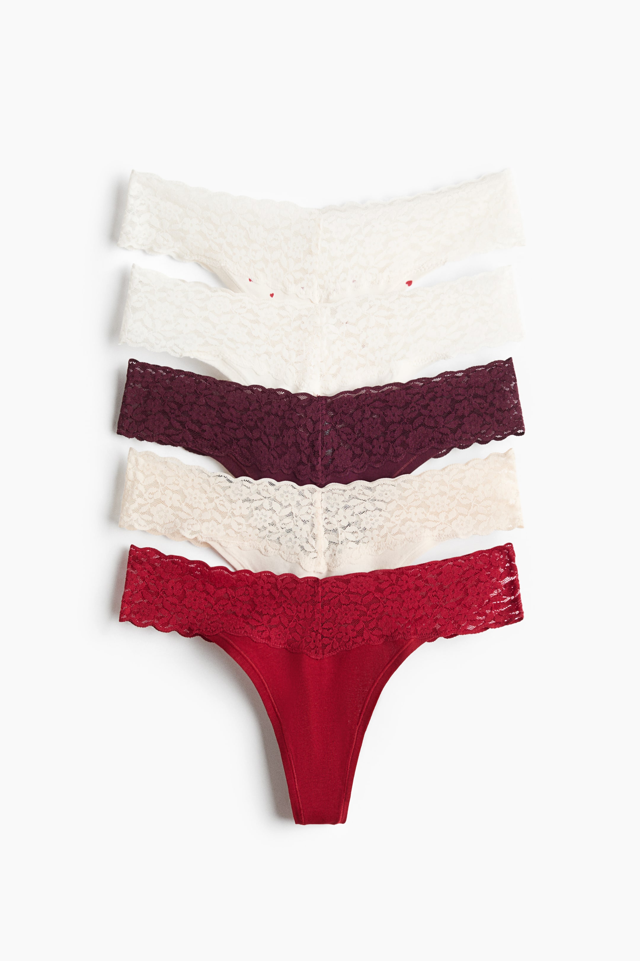 View larger image: A five-pack of lace G-string underwear is laid flat, facing front in a vertical stack. Each pair features a low, V-shaped waist made of floral lace, narrow sides, and a solid lined gusset, shown in shades of white, cream, dark burgundy, light beige, and red.