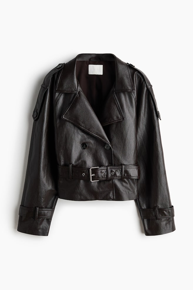 A dark brown faux leather jacket showcases its double-breasted front, featuring wide lapels, shoulder epaulettes, and a matching belt with a silver-toned buckle at the waist. Long sleeves complete the design with adjustable buckled cuffs. - 1