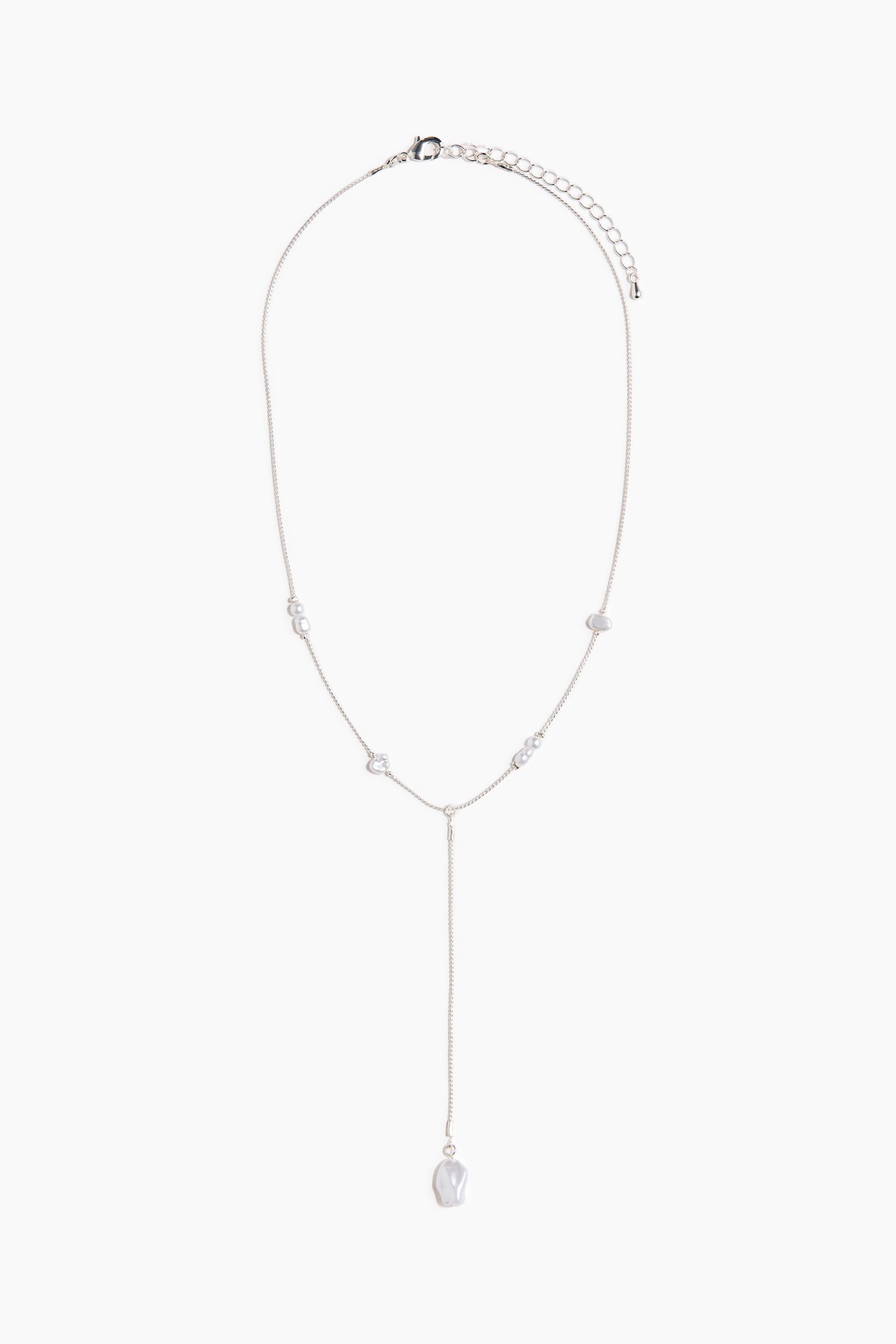 拡大画像を表示: 銀色のトーンのYネックレスが平らに置かれ、その正面を見せています。細いチェーンに不規則な白いビーズと小さな透明ビーズが間隔をあけて配置されており、長いドロップには大きな不規則な白いビーズが端に垂れ下がっています。ロブスタークラスプとエクステンダーチェーンが上部に見えます。