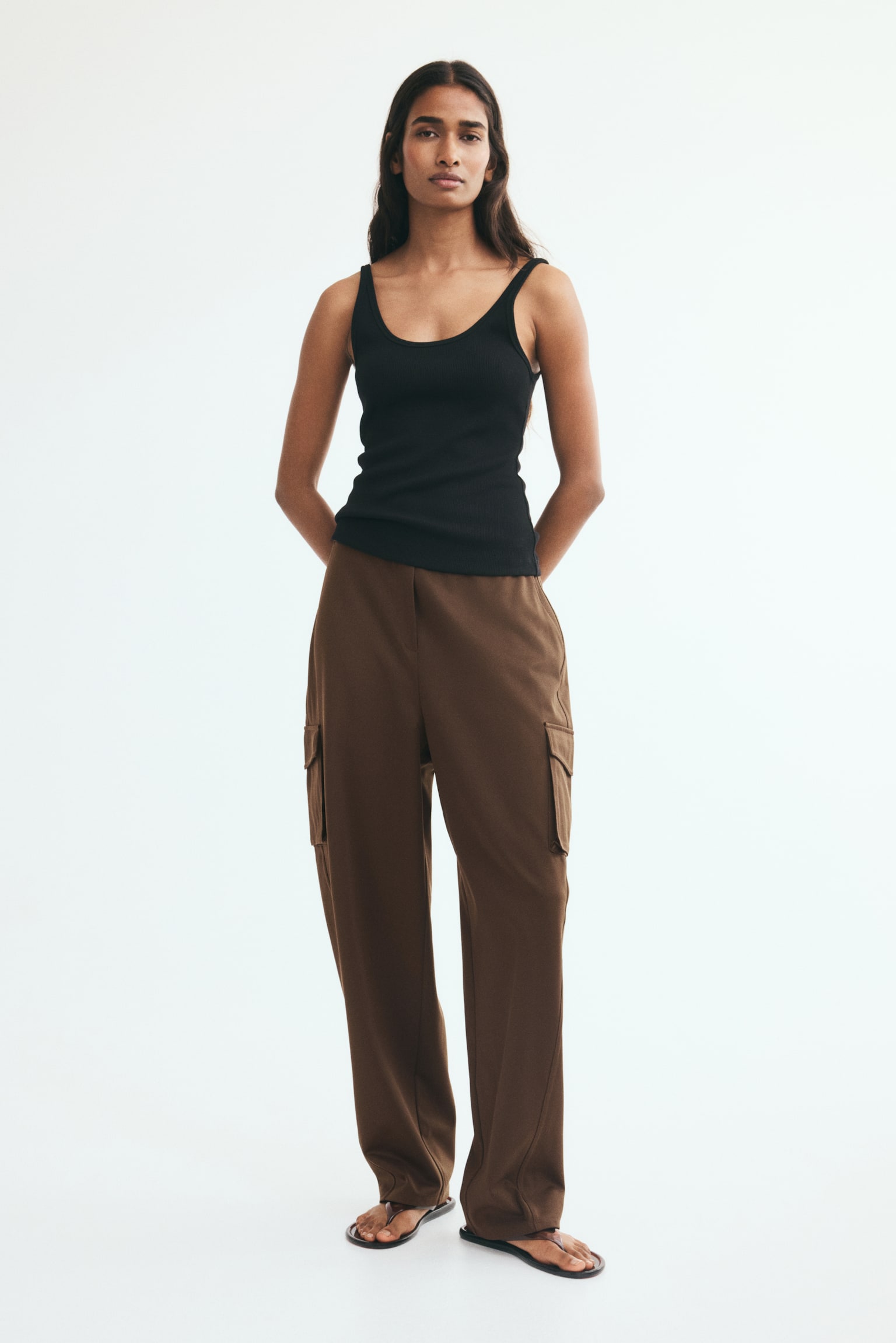 Brown cargo trousers feature a flat waistband, two hip pockets, and two large flap cargo pockets positioned on the outer sides of the legs. The trousers present a relaxed, straight-leg cut. - 1