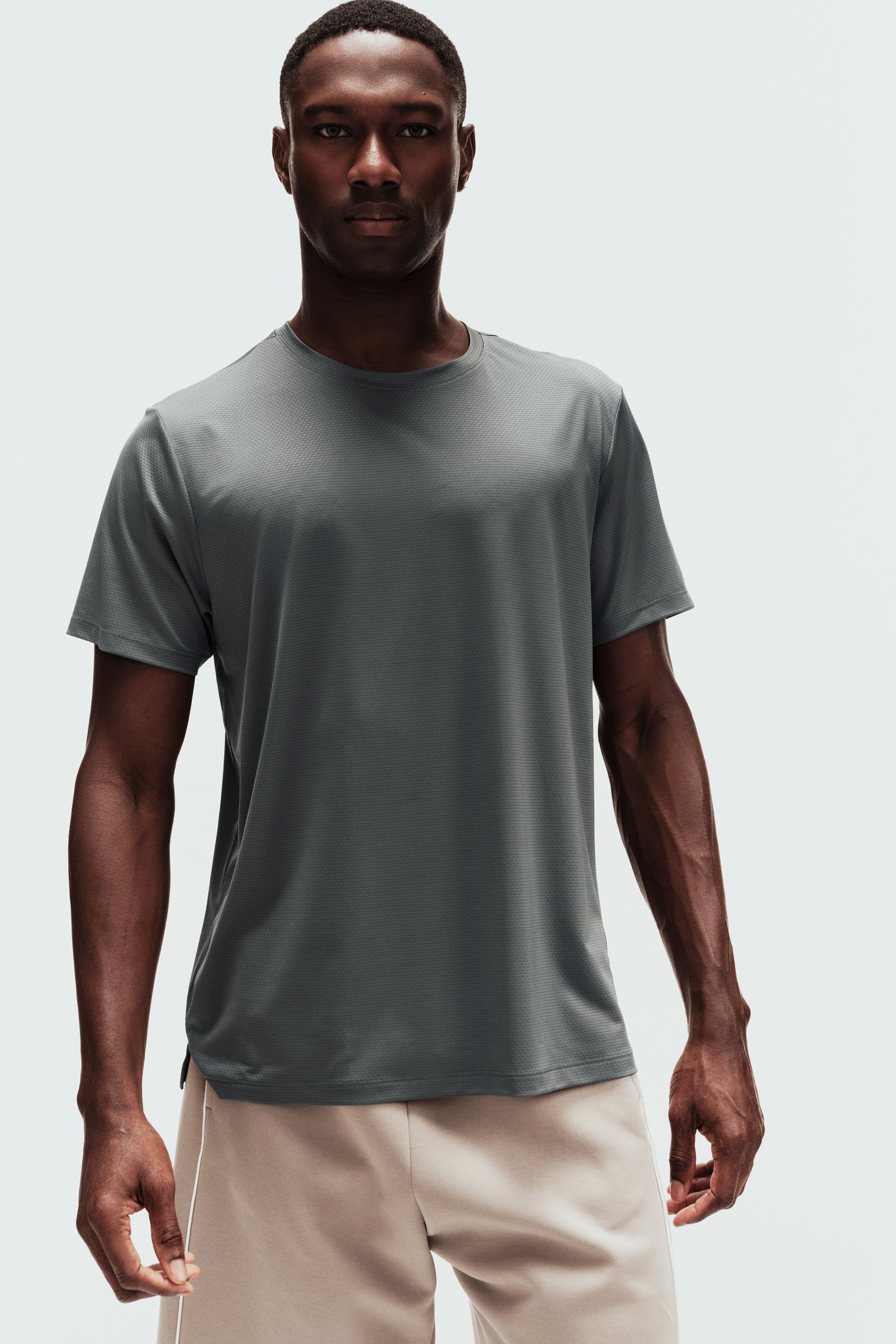 View larger image: A dark grey tee with a subtle geometric knit pattern is worn facing forward. It features a crew neck, short sleeves, and a straight hem with small side slits.