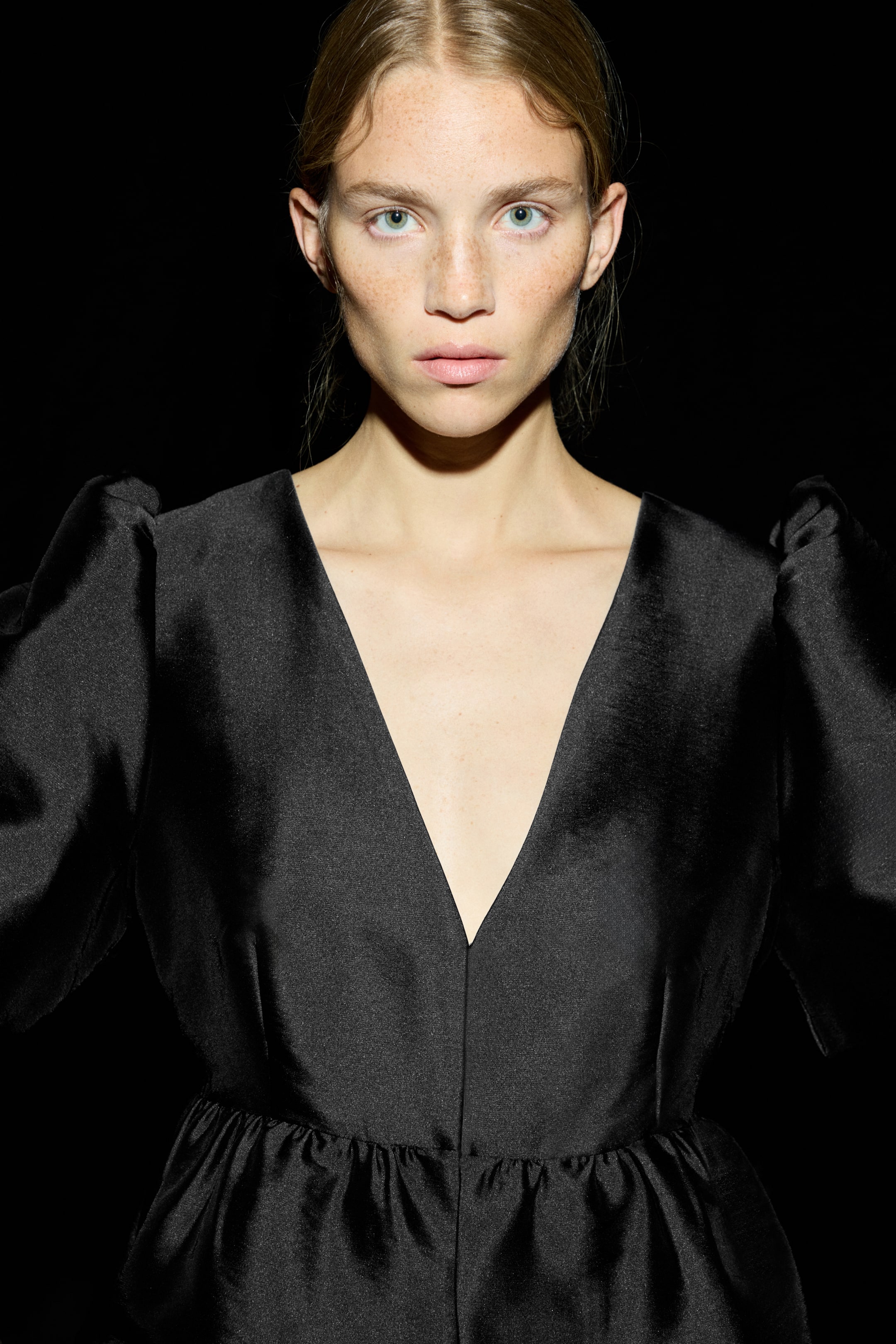 View larger image: A black top is featuring a deep V-neckline and voluminous puff sleeves, gathered at the shoulders. Its fitted bodice is transitioning into a gathered peplum at the waist, as it is presented facing forward.