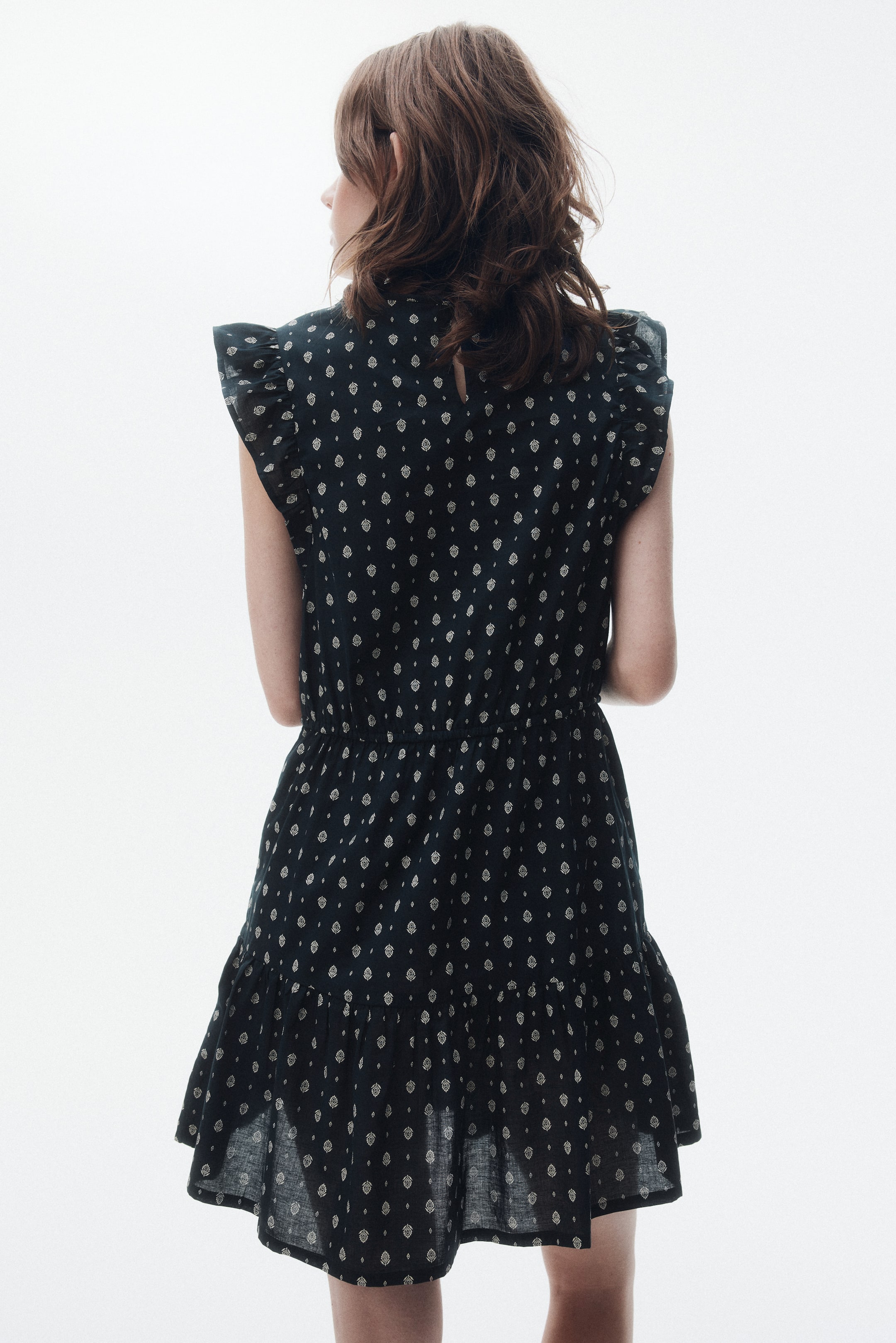 Xem ảnh lớn hơn: Một chiếc váy mini màu xanh hải quân đậm đang được giới thiệu từ phía sau, có họa tiết trừu tượng màu xám nhạt phủ khắp nơi. Nó được thiết kế với tay áo ngắn xếp nếp, eo bó chun và váy phân tầng với viền xếp nếp.