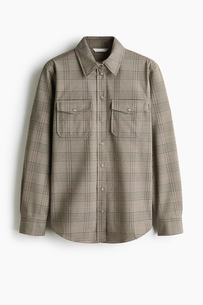 Une surchemise à manches longues présentant un motif à carreaux Glen marron et beige est vue de face, mettant en valeur un col pointu et une fermeture boutonnée sur le devant. La chemise est conçue avec deux poches poitrine à rabat boutonnées, des manches longues avec poignets boutonnés et un ourlet arrondi. - 1