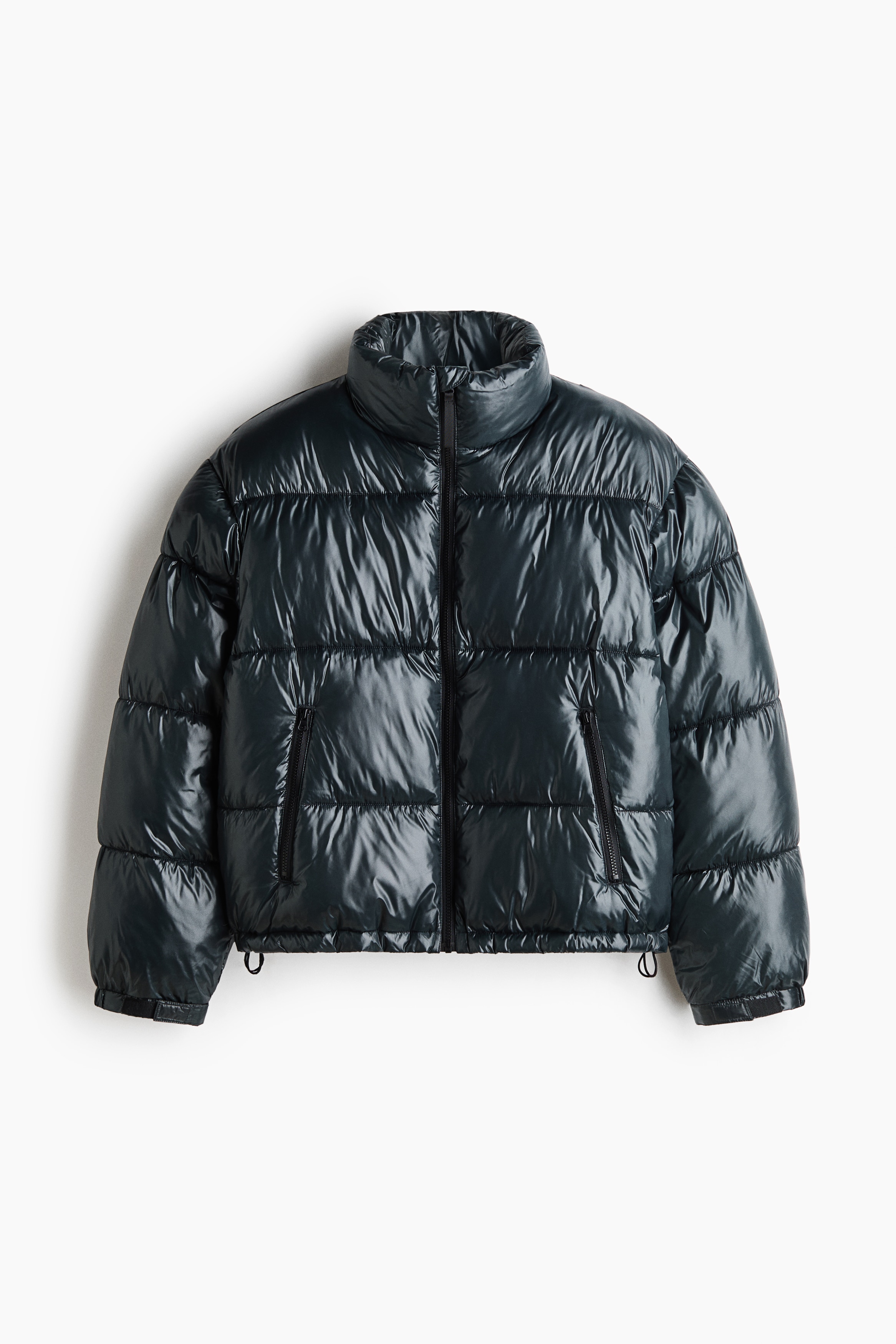 Un blouson matelassÃ© noir Ã  lâaspect lustrÃ©, dotÃ© dâun col montant et dâune fermeture Ã©clair Ã  lâavant, est portÃ© par le mannequin. Le blouson est stylÃ© avec un pantalon foncÃ© ample et des espadrilles assorties.