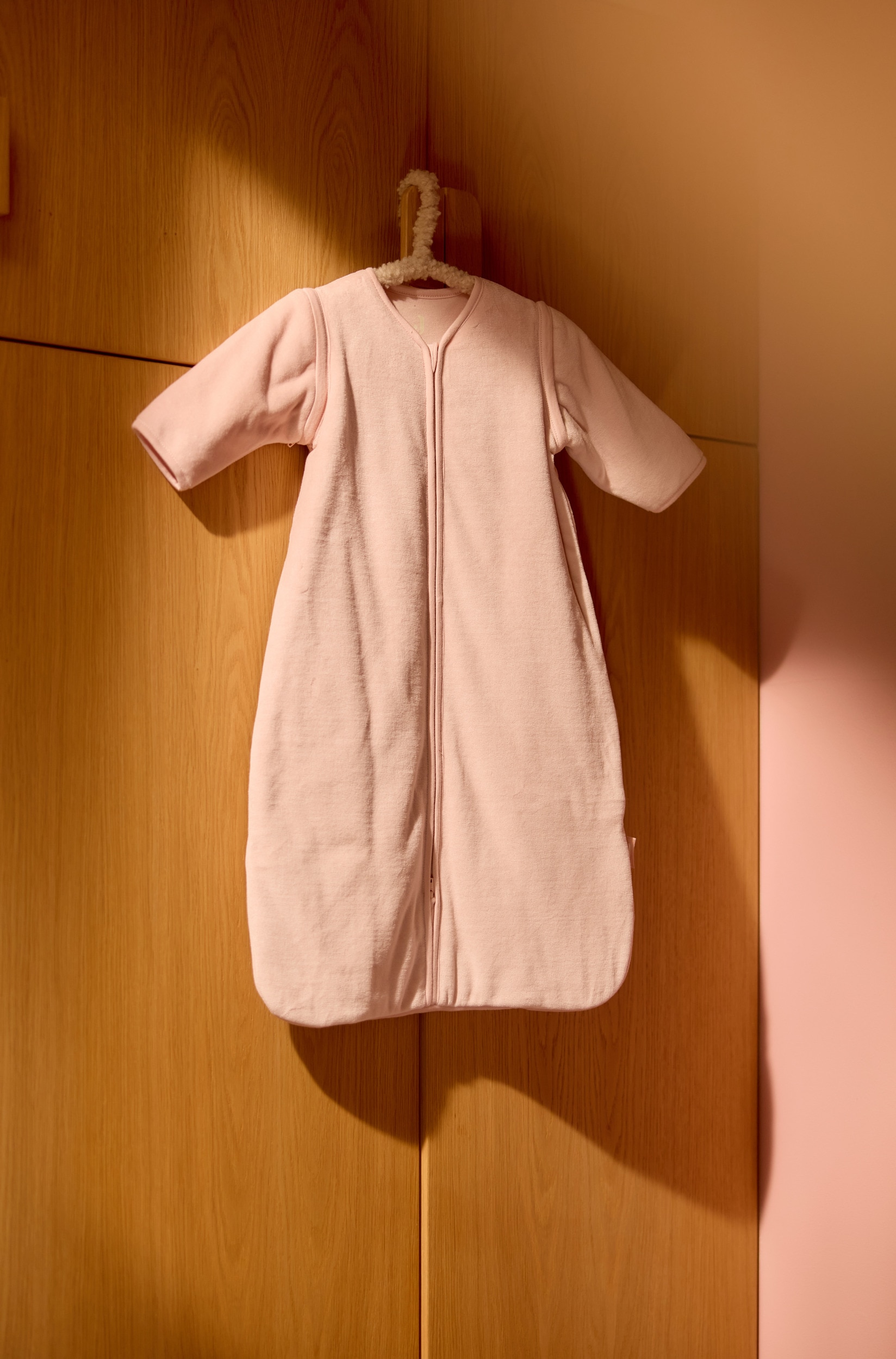 Ein hellbeiger, flauschiger Babyschlafsack liegt flach und ist nach vorne ausgerichtet. Er verfügt über lange Ãrmel, einen durchgehenden ReiÃverschluss in der Mitte und einen abgerundeten Halsausschnitt; er läuft nach unten hin in einen breiten, abgerundeten Saum aus.