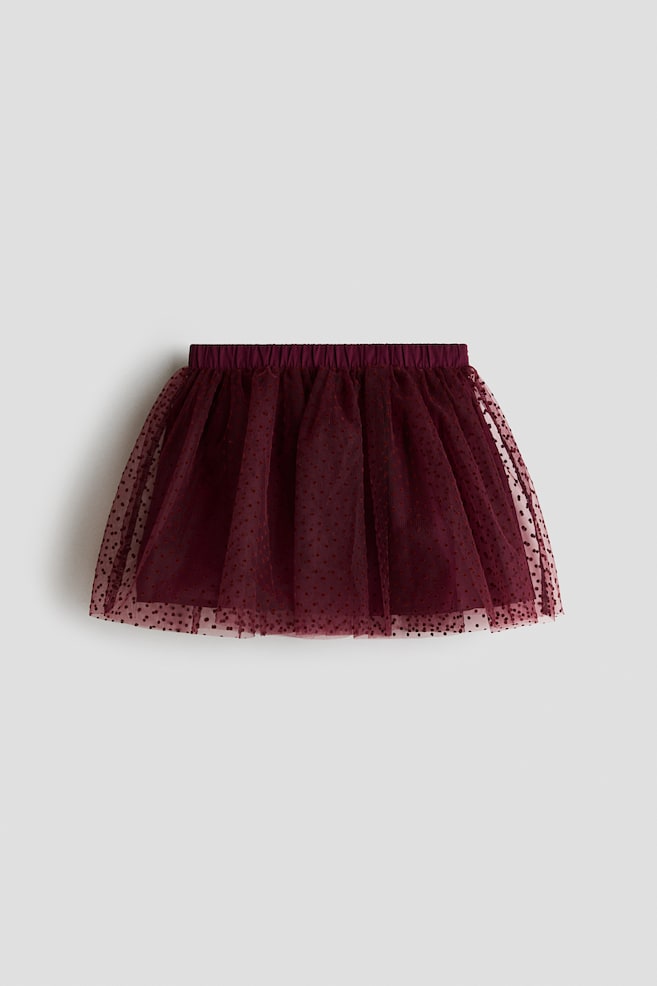 Ein dunkelroter ausgestellter Tüllrock ist von vorne zu sehen, mit einem durchgängigen flockierten Punktmuster und einem elastischen Bund. Die transparente äuÃere Tüllschicht ist an der Taille gerafft und fällt über ein blickdichtes, farblich abgestimmtes Futter. - 1