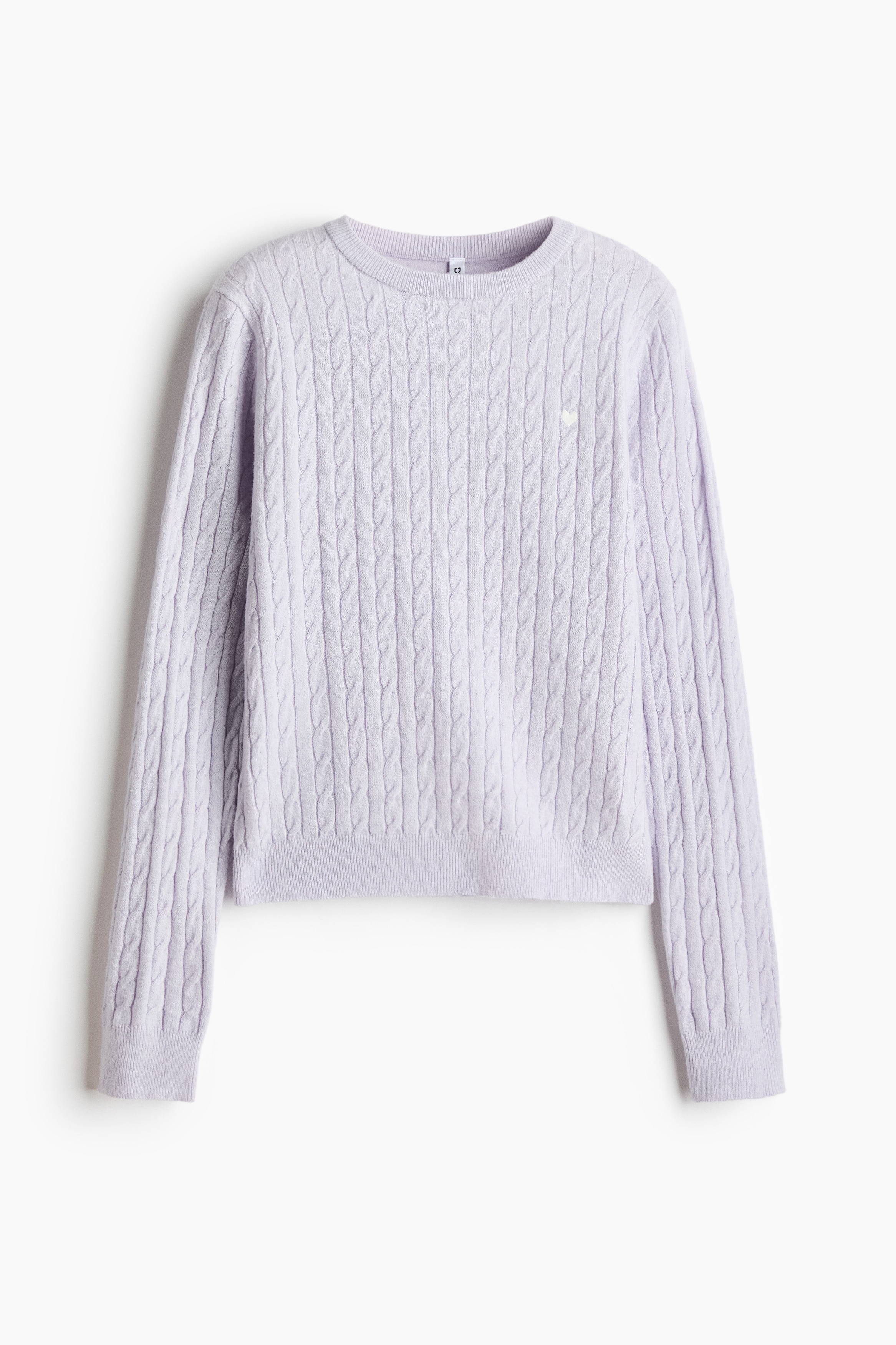 A light purple cable-knit jumper with a round, rib-trimmed neckline is being worn by the model over a white crew-neck top. The jumper features long sleeves and a small, white embroidered heart on the chest.