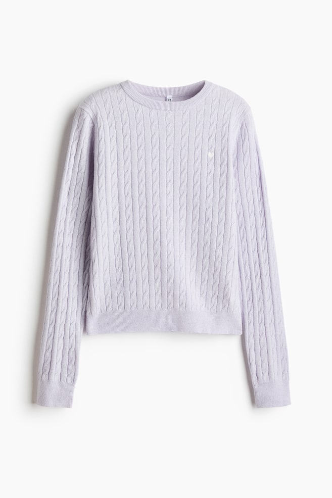 A light purple cable-knit jumper is shown from the front, featuring an all-over vertical cable pattern, a ribbed crew neck, ribbed cuffs, and a ribbed hem. A small white embroidered heart details the upper left chest. - 1