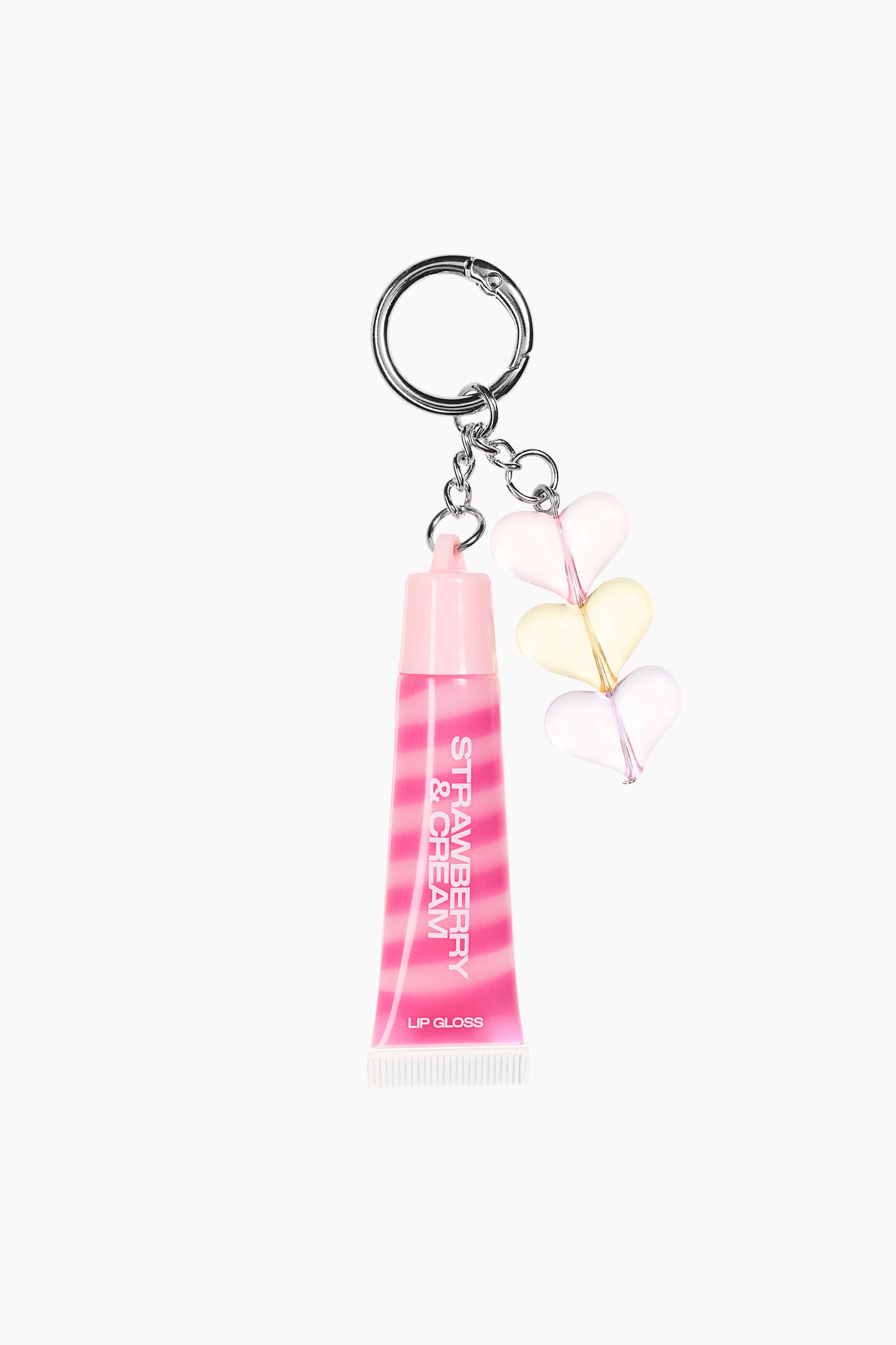 View larger image: A lip gloss charm features a miniature lip gloss tube with pink and white swirl stripes and "STRAWBERRY & CREAM LIP GLOSS" text on its front. It's accompanied by three stacked heart charms in light pink, light yellow, and clear, all attached to a silver-toned key ring.